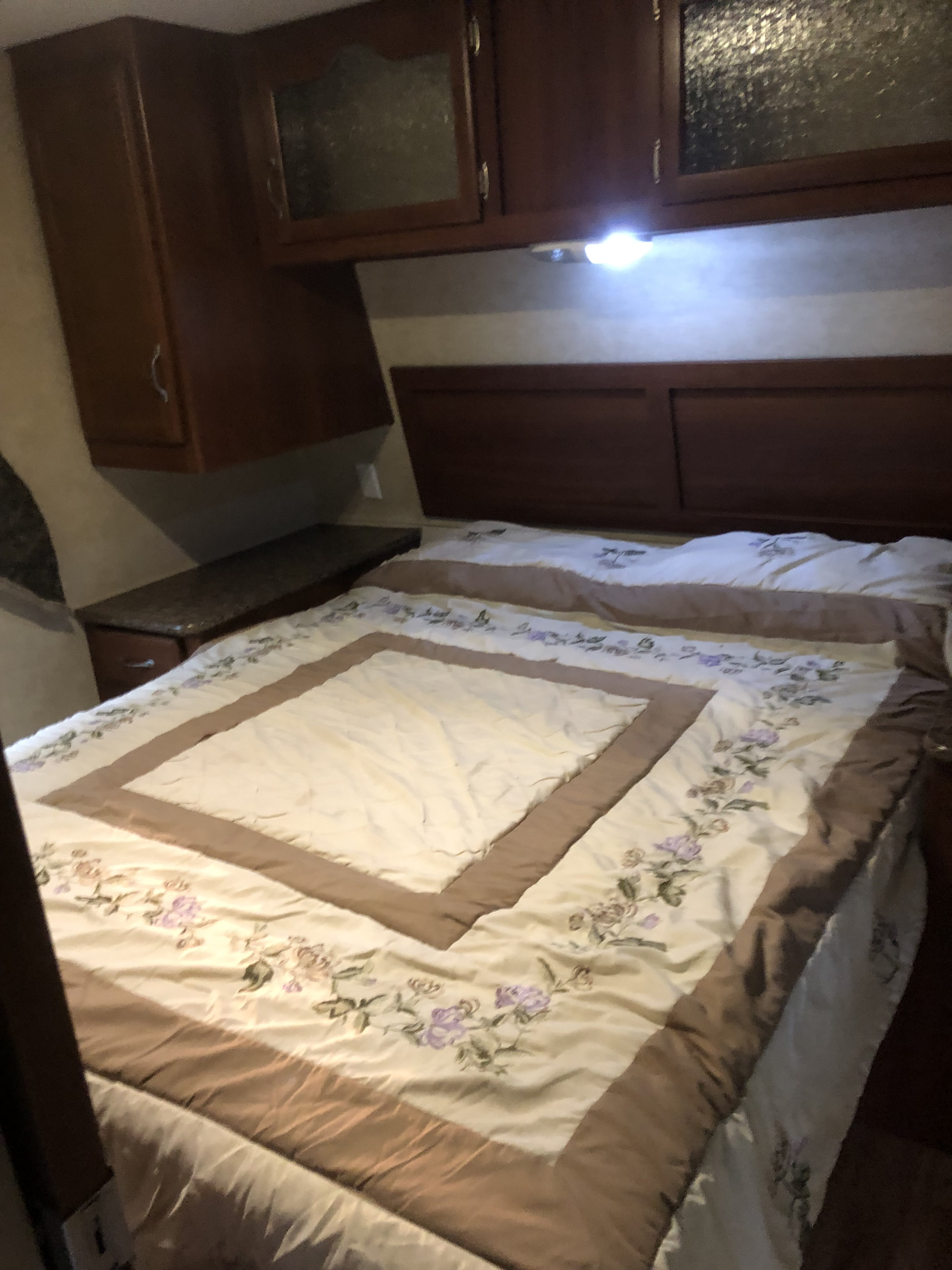 Cozy RV rental bedroom featuring dark wood cabinets, a floral bedspread, and a sturdy headboard.. Outdoors RV Timber Ridge 2011