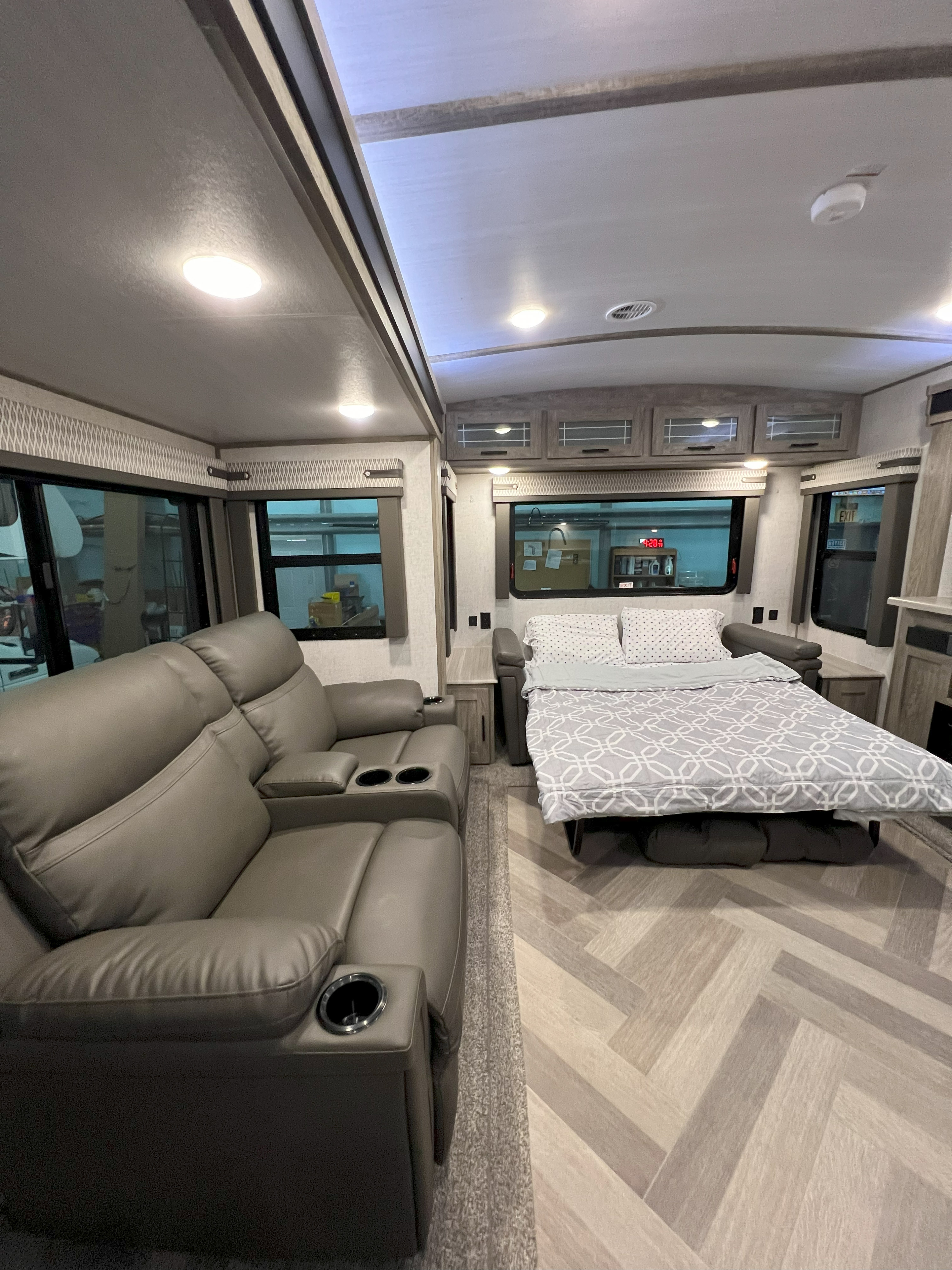 Interior of a modern RV rental, featuring a gray reclining sofa on the left and a pull-out bed on the right.. Forest River Wildwood Heritage Glen 2021