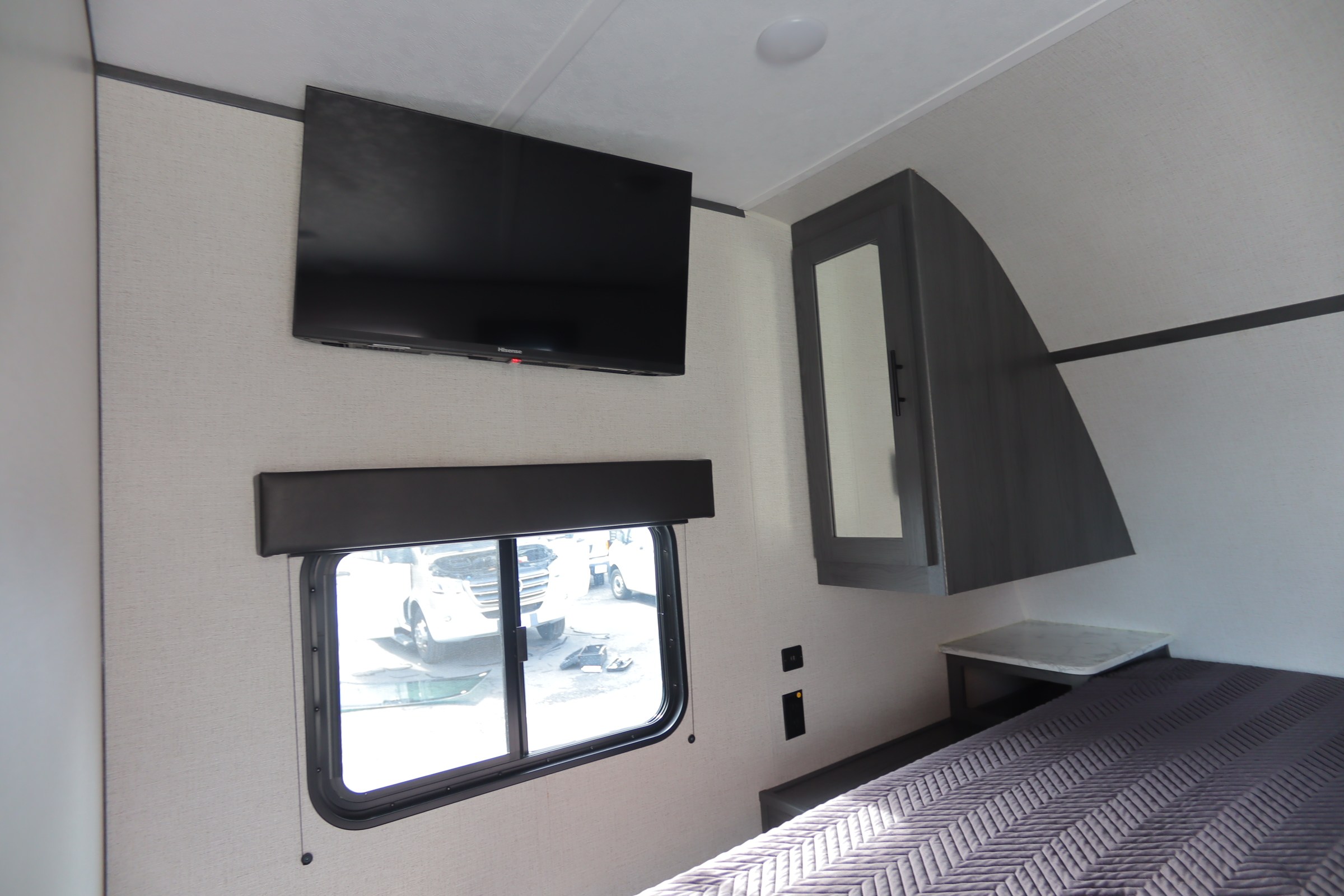 Inside an RV rental bedroom: mounted Hisense TV, window, dark storage cabinet, and quilted bed.. Dutchmen Aspen Trail 2022