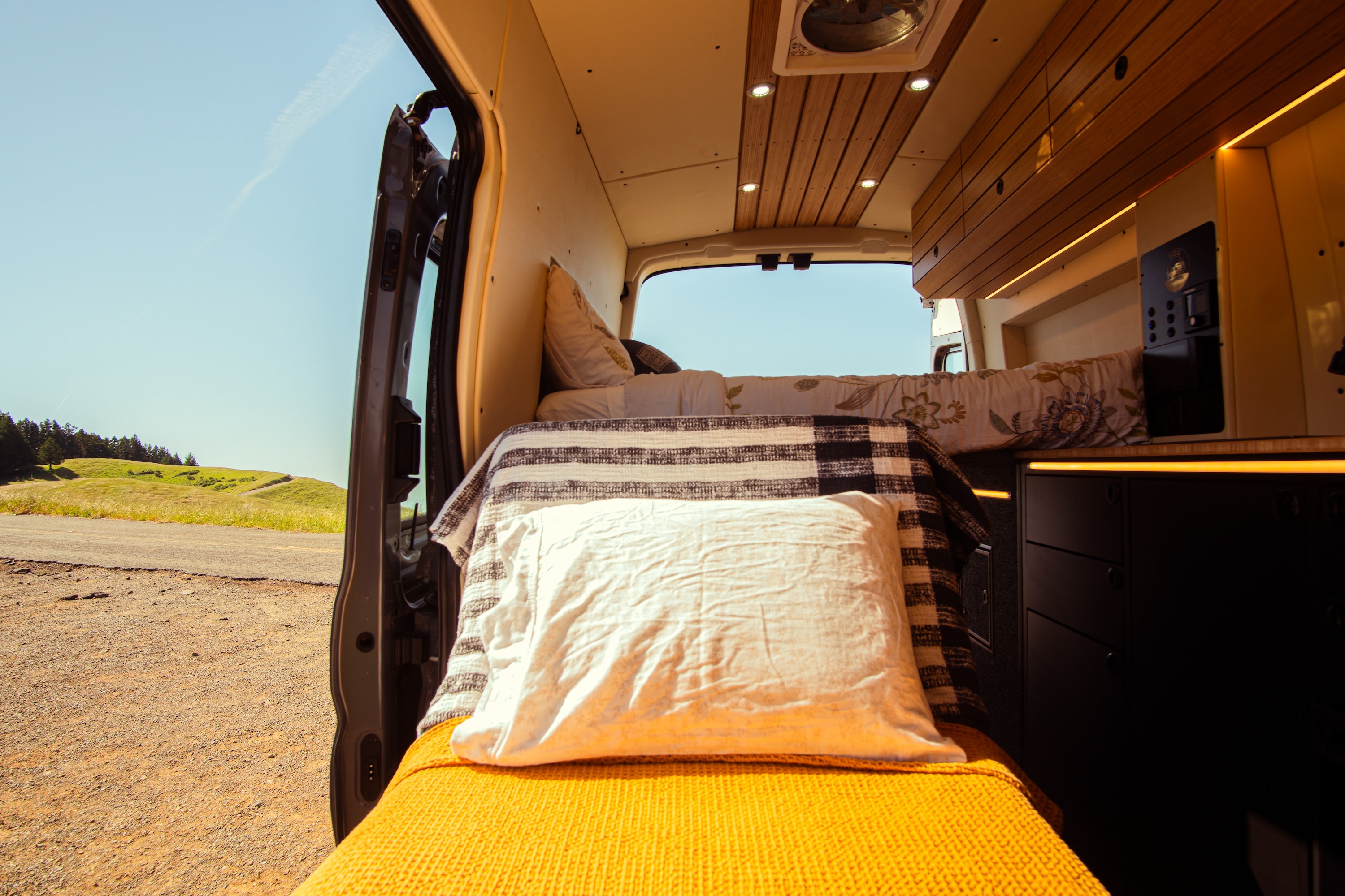 Cozy RV rental interior with a bed and outdoor views of green hills and blue sky from the open side door.. Ford Transit 2023