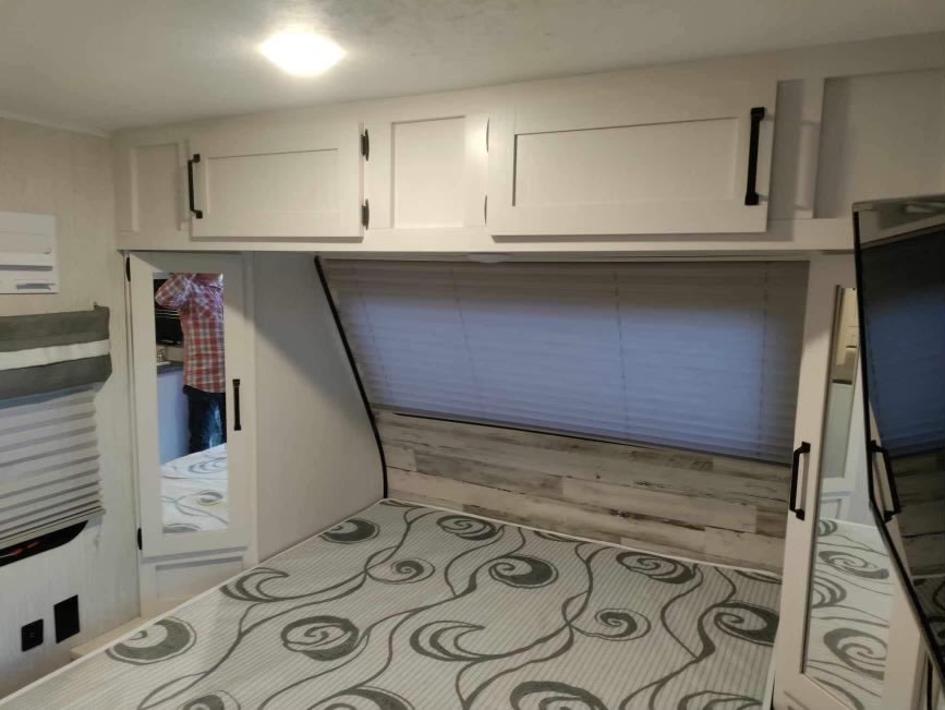 Inside an RV rental bedroom: cozy bed, overhead cabinets, and mirror. Perfect for your mobile travel adventure.. Forest River Puma Ultralite Palomino 2021