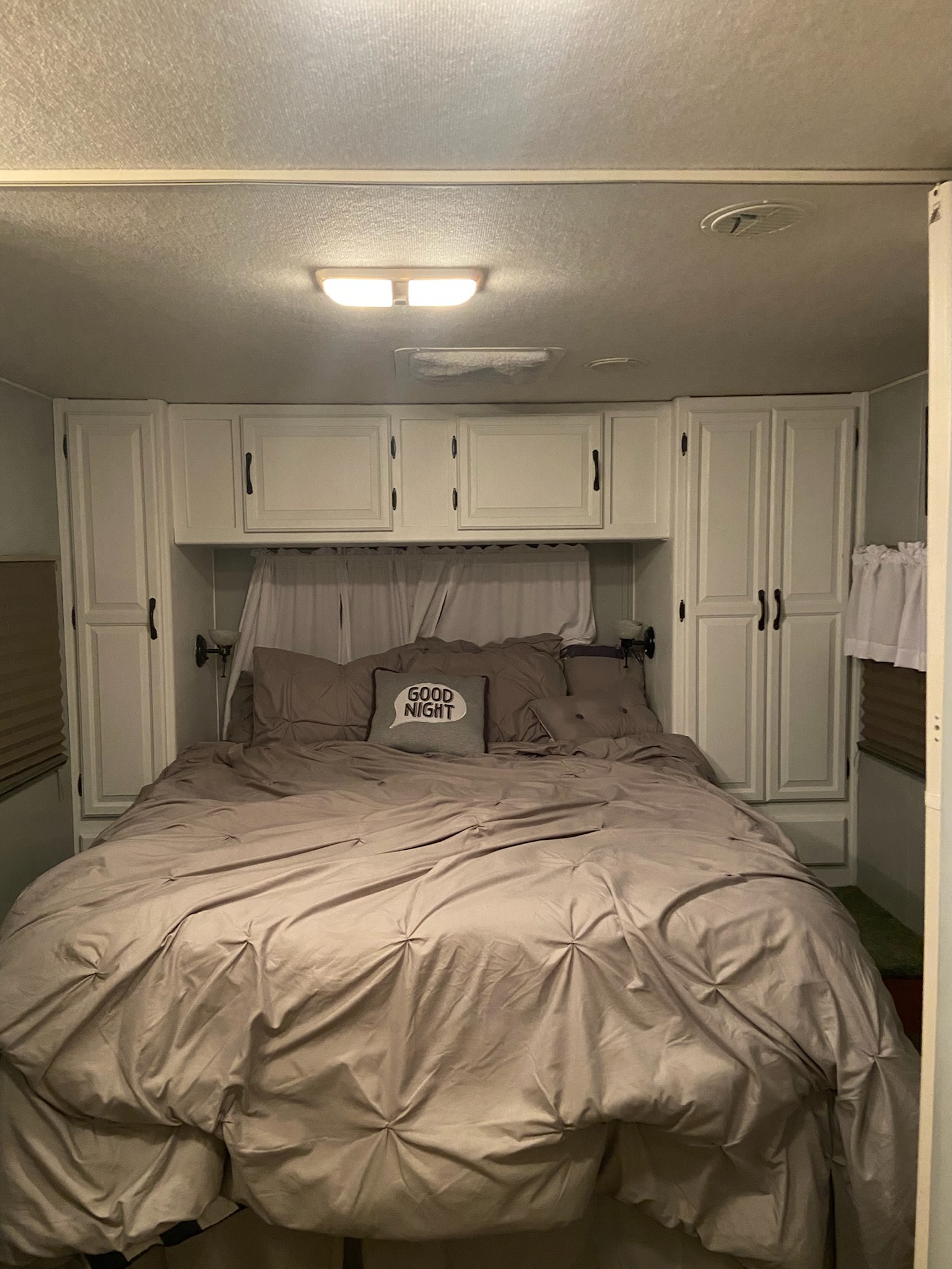 This cozy RV rental bedroom features a bed with soft taupe bedding, white storage cabinets, and overhead lighting.. Coachmen Santara 2002