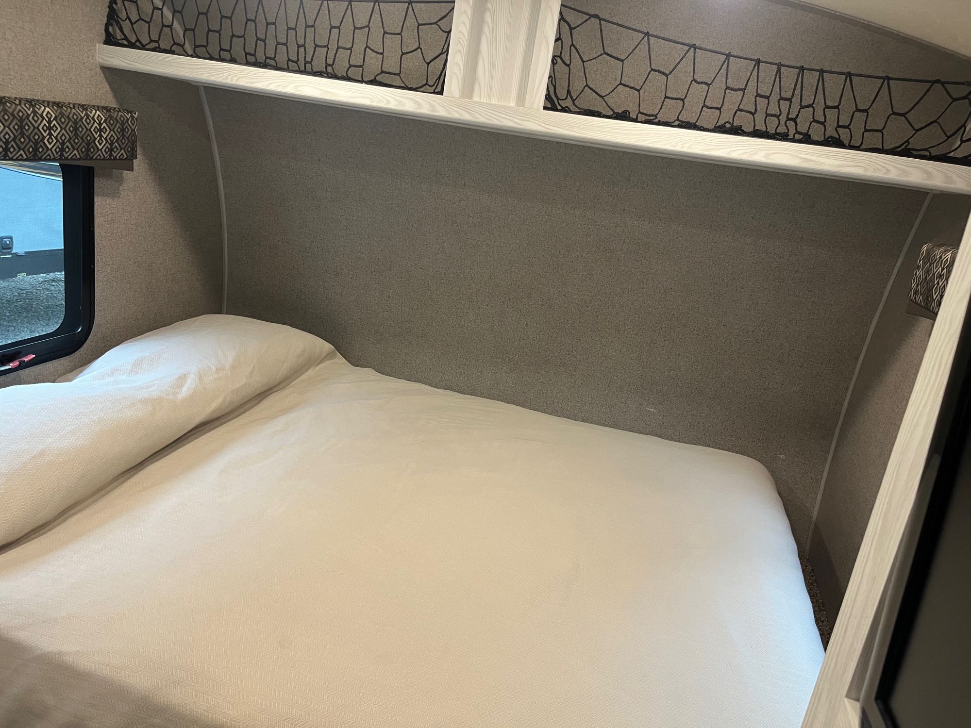 Interior of an RV rental bedroom, featuring a white bed, side window, and netted overhead storage.. Forest River Flagstaff E-Pro 2018
