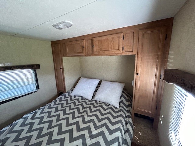 Inside an RV rental: a compact bedroom with a chevron bed, overhead cabinets, and side closets. Bright and functional.. Skyline Weekender 2012