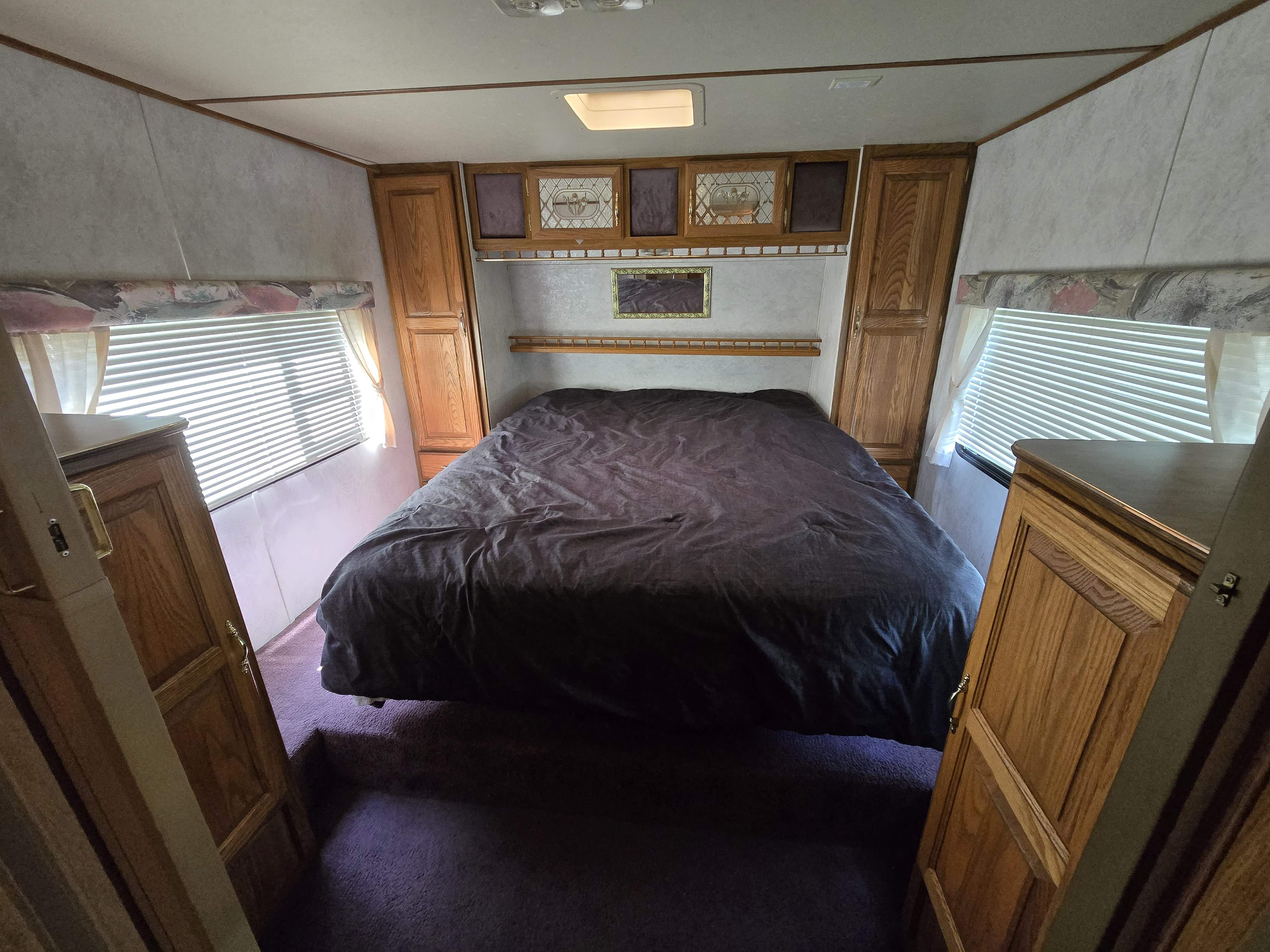 RV rental bedroom interior features a large bed, wooden storage, and bright windows, offering cozy travel accommodations.. Dutchmen Royal Classic 1995