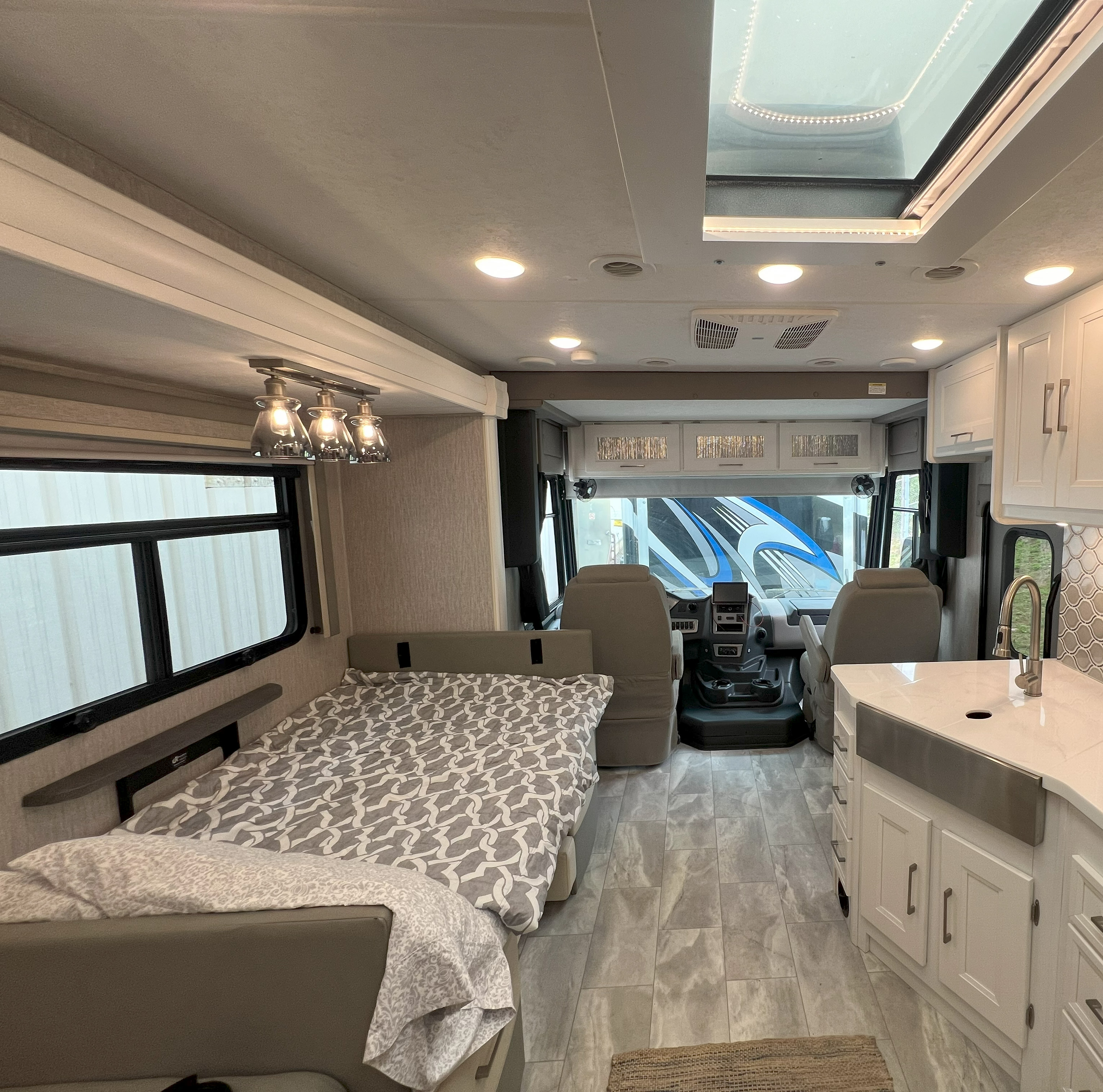 Modern RV rental interior, showing a cozy bed, sleek kitchen, and front cockpit. A bright, comfortable travel space.. Coachmen Encore 2021
