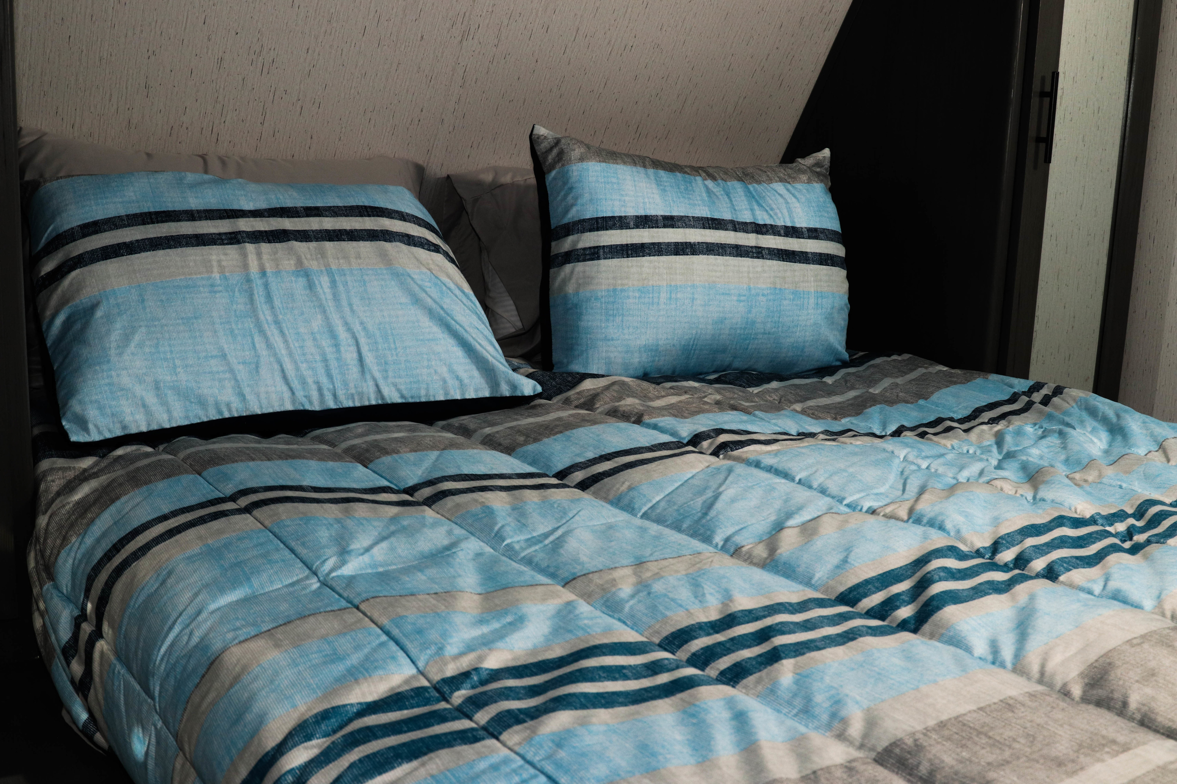 Cozy bed with blue and grey striped bedding in an RV rental, perfect for a comfortable night's sleep.. Dutchman Aspen Trail LE 2024