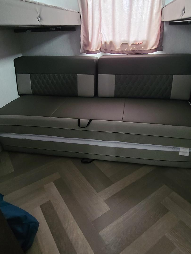 RV rental interior shows a grey convertible seating area with quilted backrests, bunk beds above, and wood flooring.. Forest River Wildwood X-Lite 2022