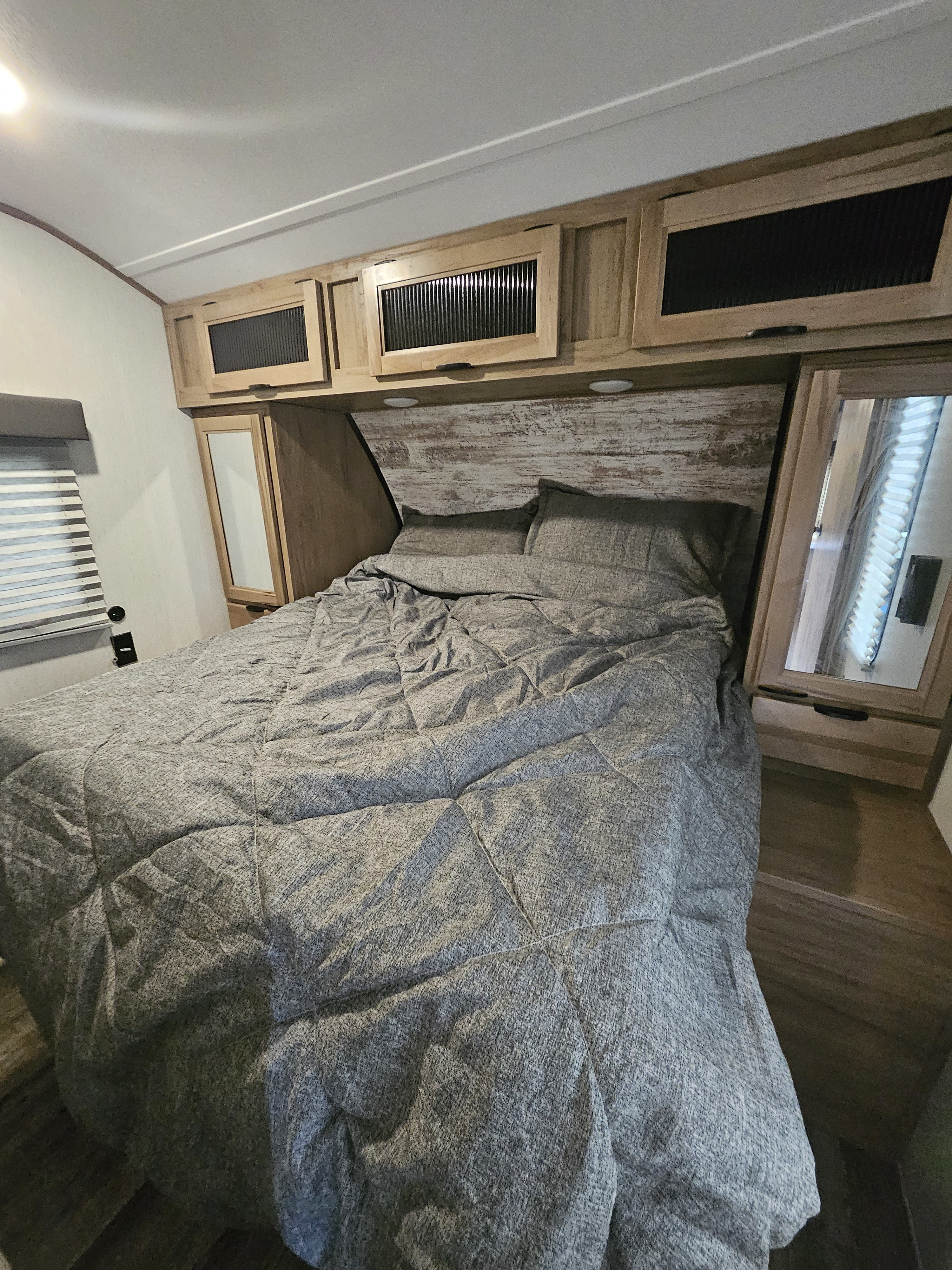 Cozy RV rental bedroom featuring gray bedding, rustic headboard, overhead cabinets, and a mirrored wardrobe.. Forest River Other 2024