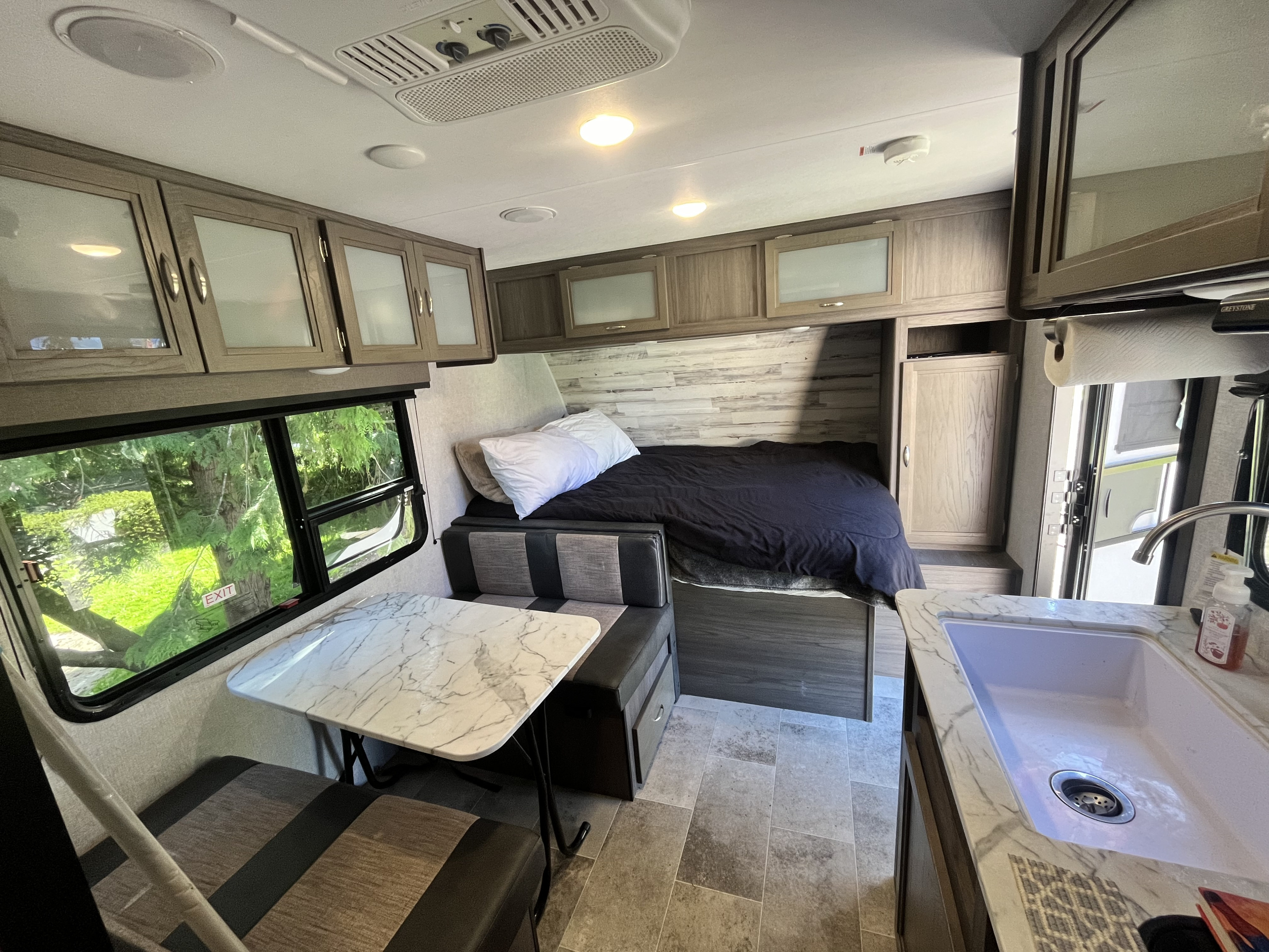 RV rental interior featuring a cozy bed, dinette, kitchen sink, and overhead cabinets.. Dutchmen Kodiak Cub 2020