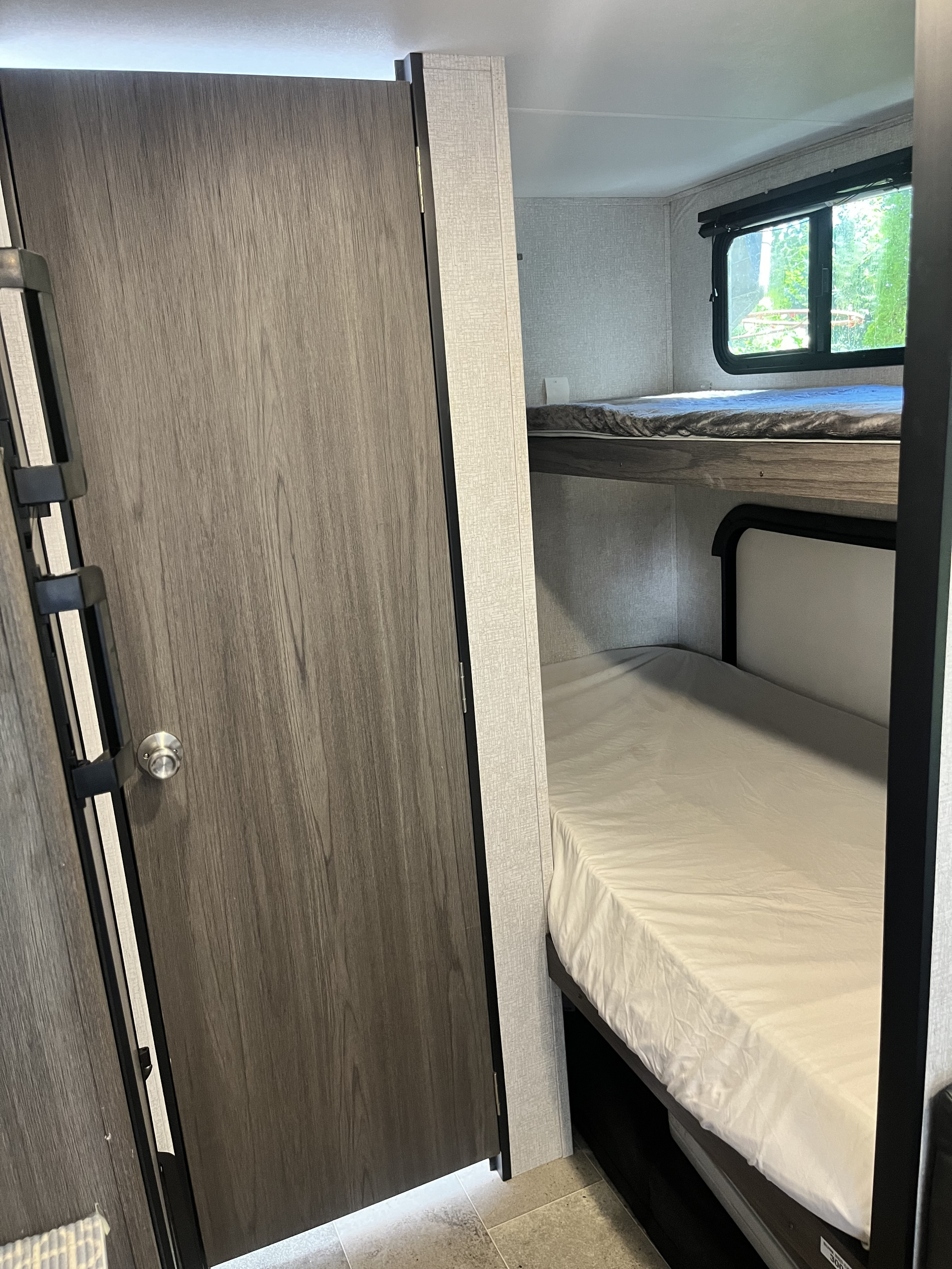 RV rental interior featuring comfortable bunk beds and a closed wood-grain door, ideal for family sleeping.. Dutchmen Kodiak Cub 2020