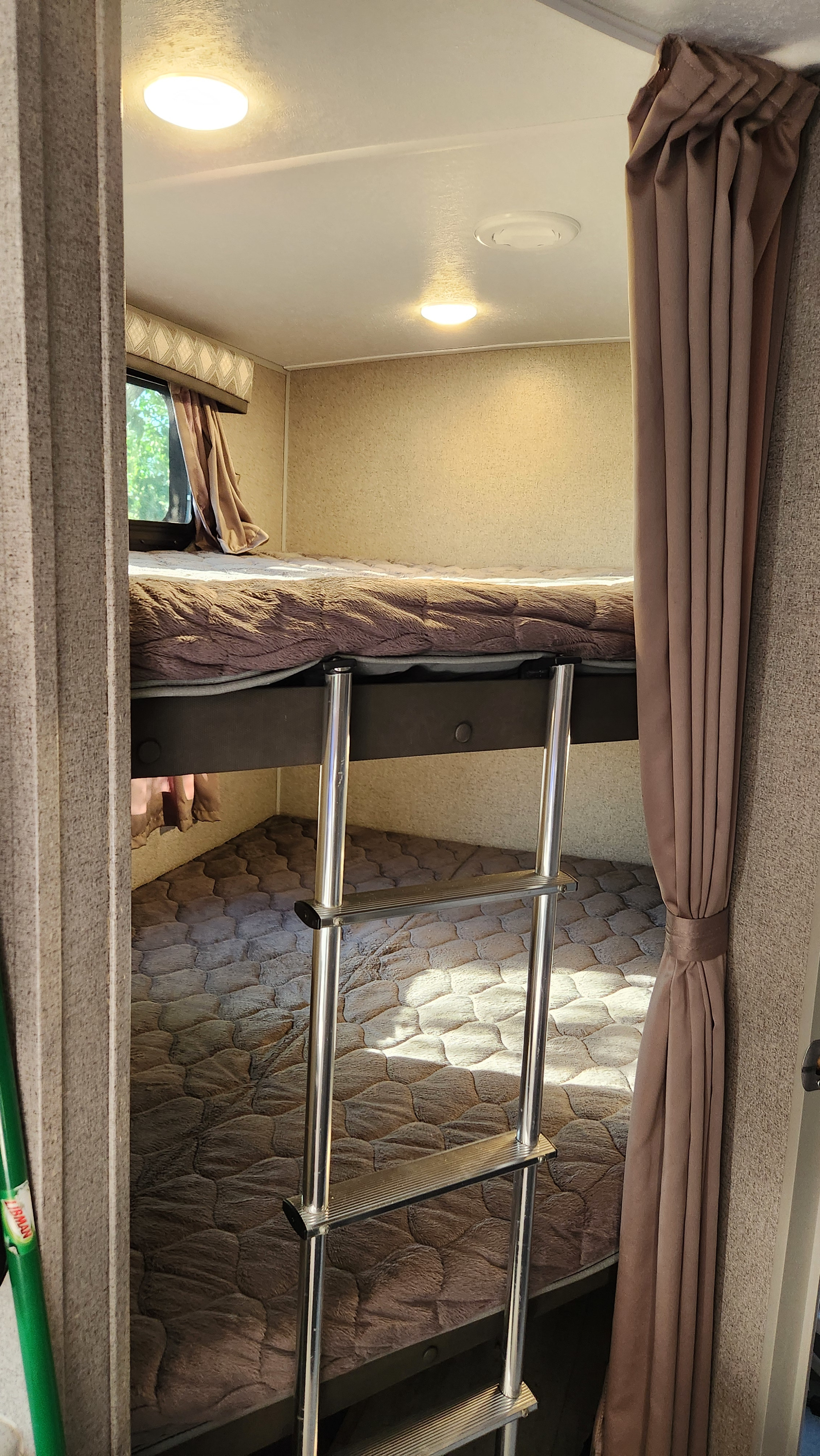 Interior of an RV rental showing cozy bunk beds with a ladder, soft bedding, and natural light from a window.. Forest River Flagstaff Micro Lite 2021