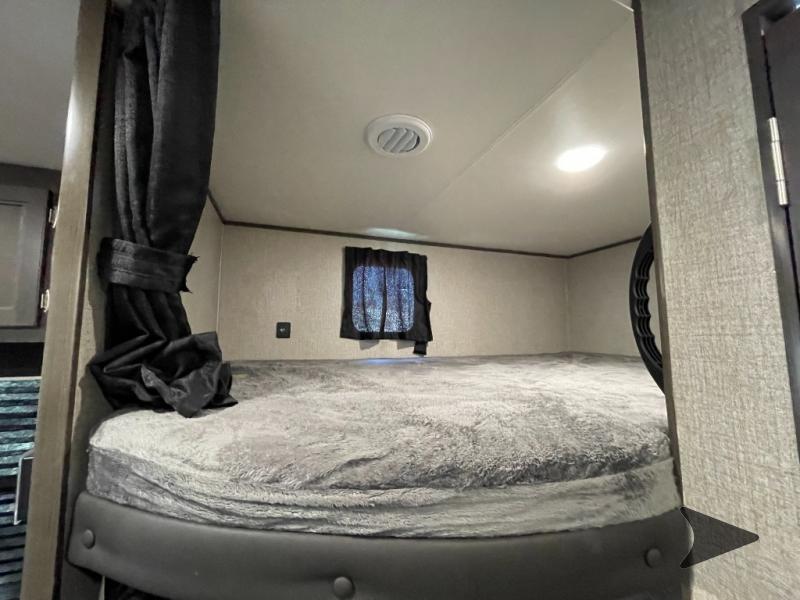 Cozy RV rental bunk bed features grey fluffy bedding, window, privacy curtain, light, and vent for travel.. Jayco Jay Flight 2022