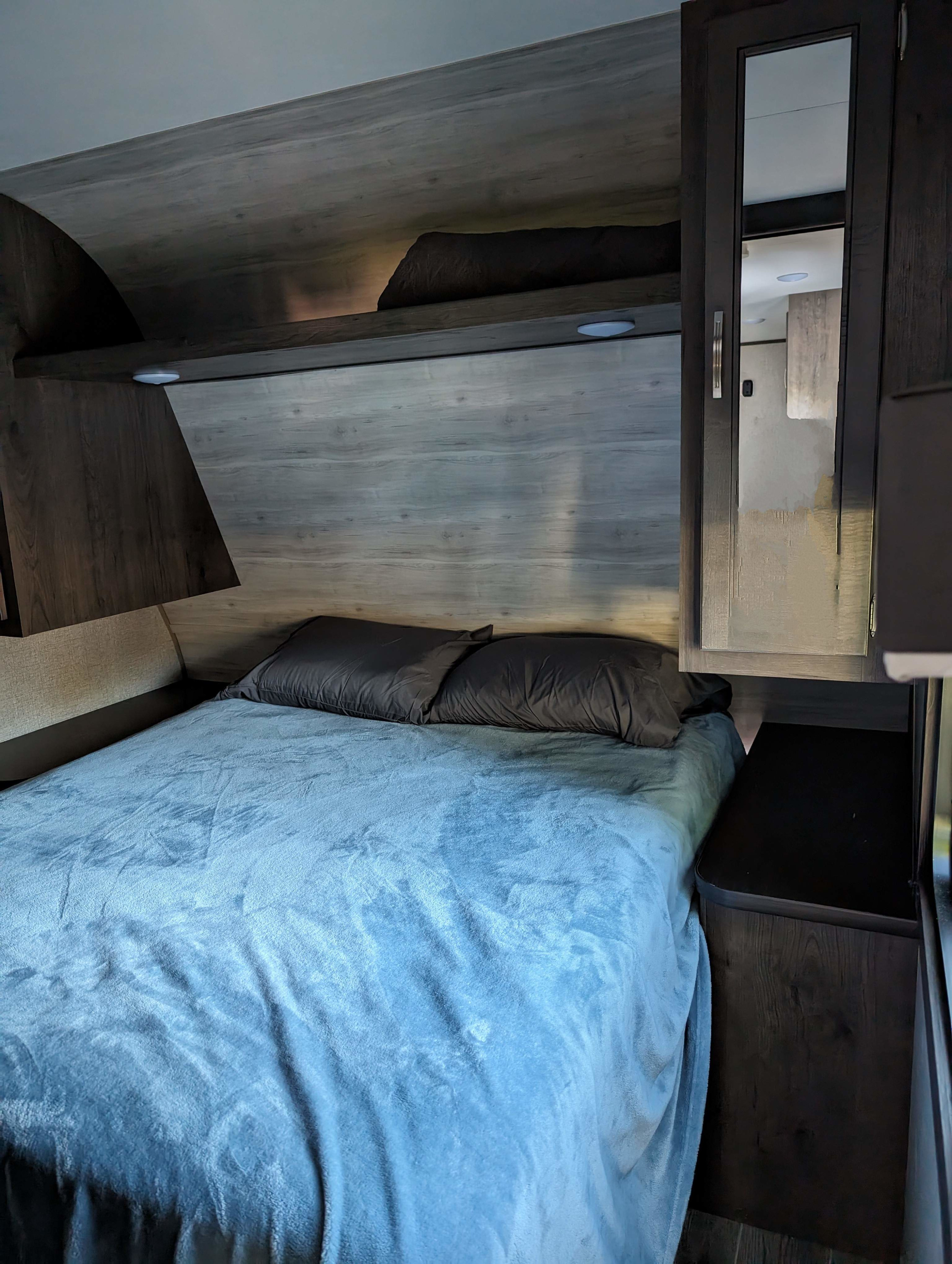 RV rental bedroom: cozy bed with blue blanket, dark pillows, wood paneling, overhead shelf, mirrored cabinet.. Jayco Jay Flight SLX 2021
