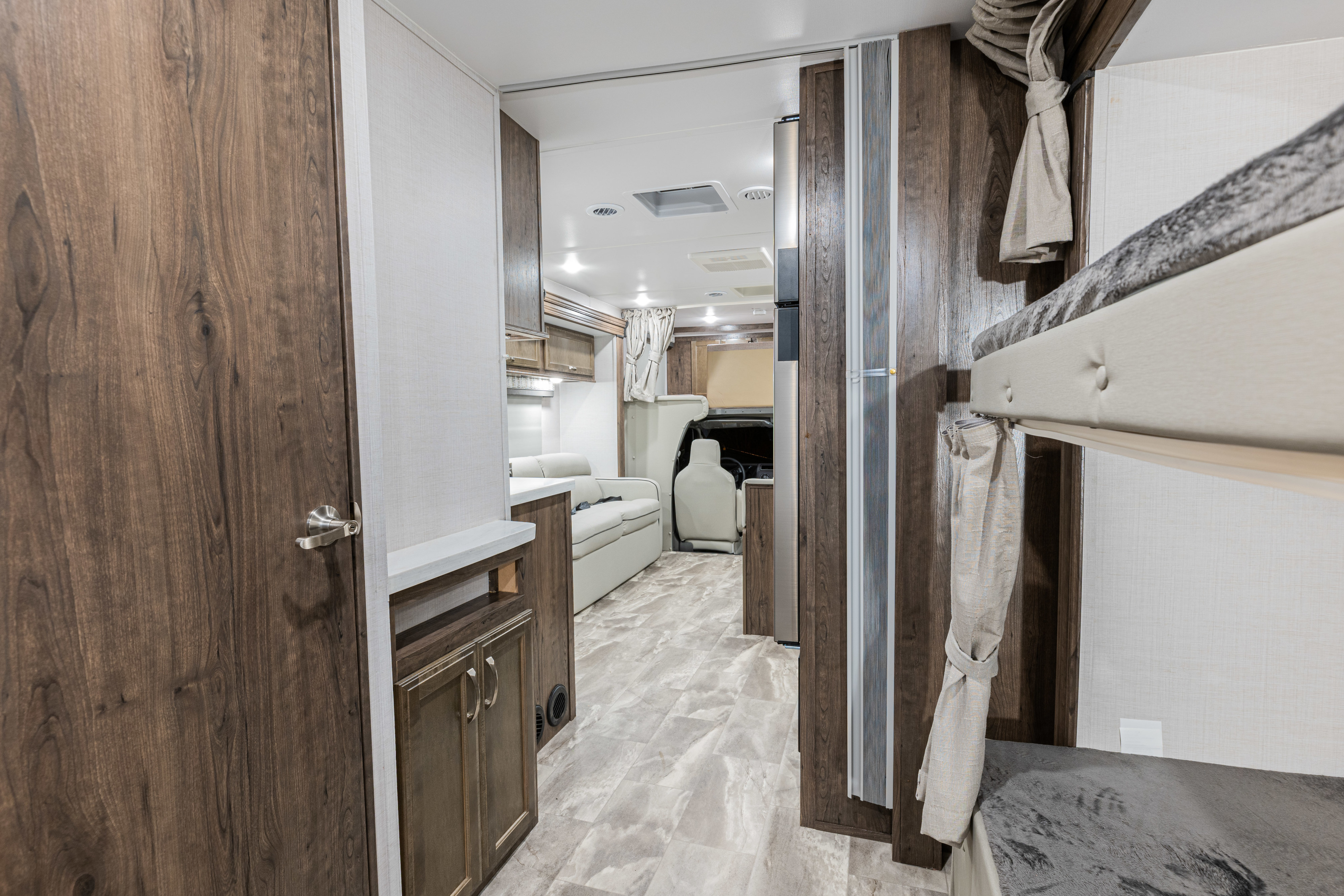 Modern RV rental interior with a hallway leading to bunk beds, wood cabinets, and cream seating.. Gulf Stream Yellowstone 2023
