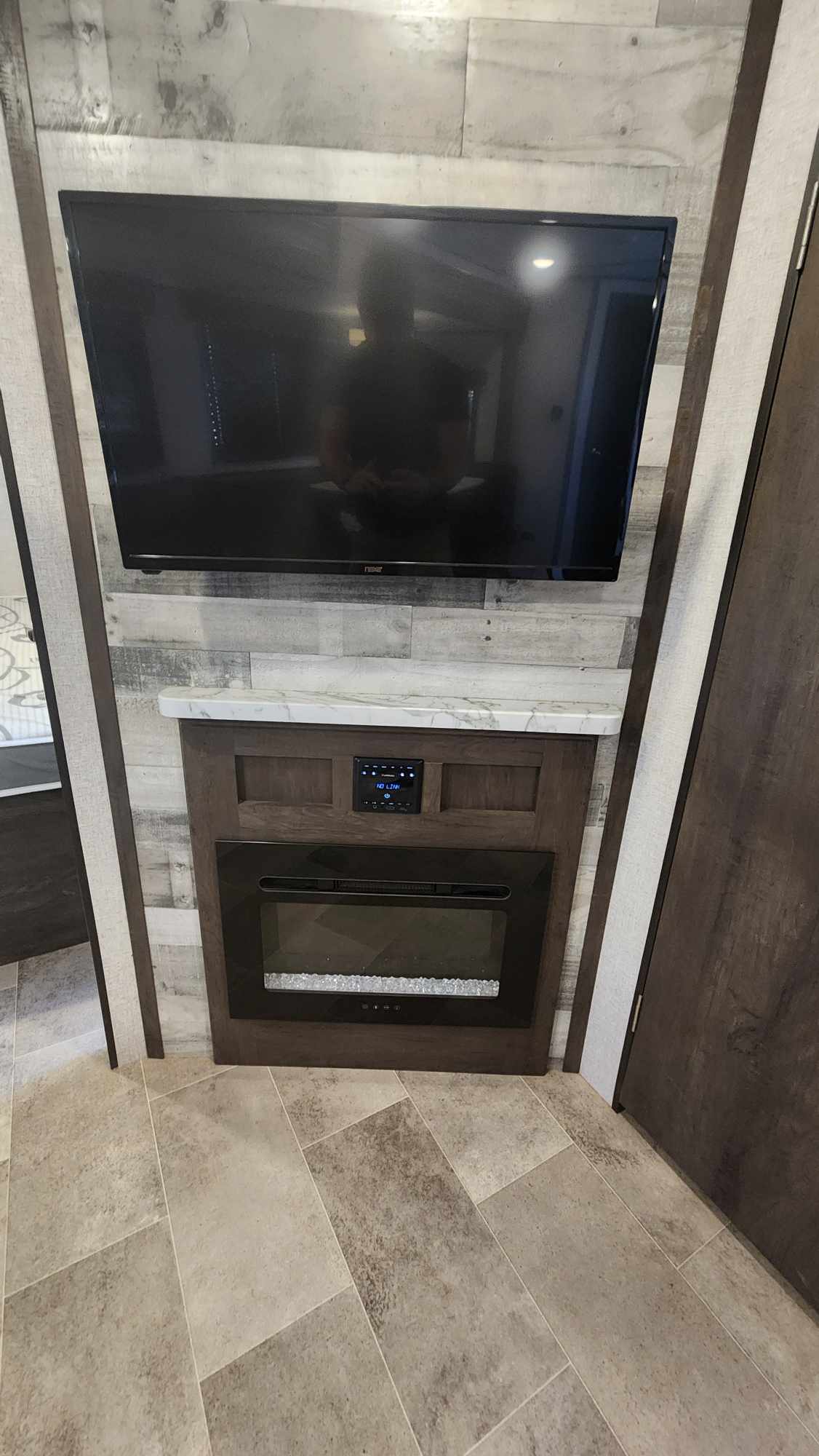 Sleek RV rental interior: TV, digital media panel, and electric fireplace on a wood-paneled wall above tiled floor.. Dutchmen Coleman Light 2021