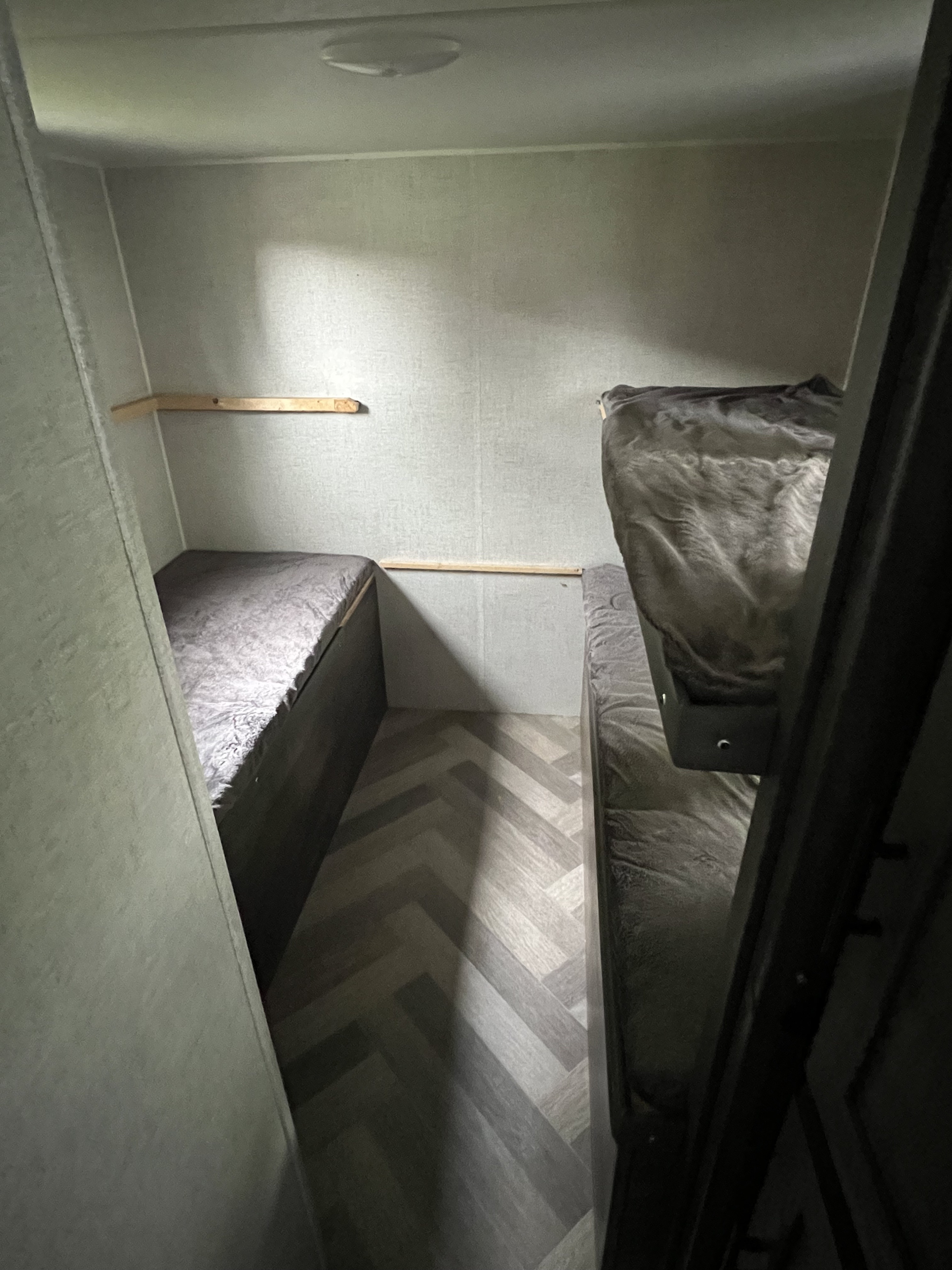 Cozy RV rental interior: herringbone floor, bunk beds, and a small wall shelf in a compact sleeping area.. Forest River X-Lite 2020