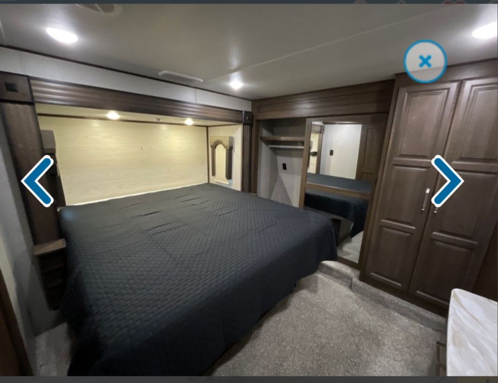 Spacious RV rental bedroom with dark quilted bed, overhead lighting, and built-in wardrobe. Ideal for travel comfort.. Keystone RV Avalanche 2020
