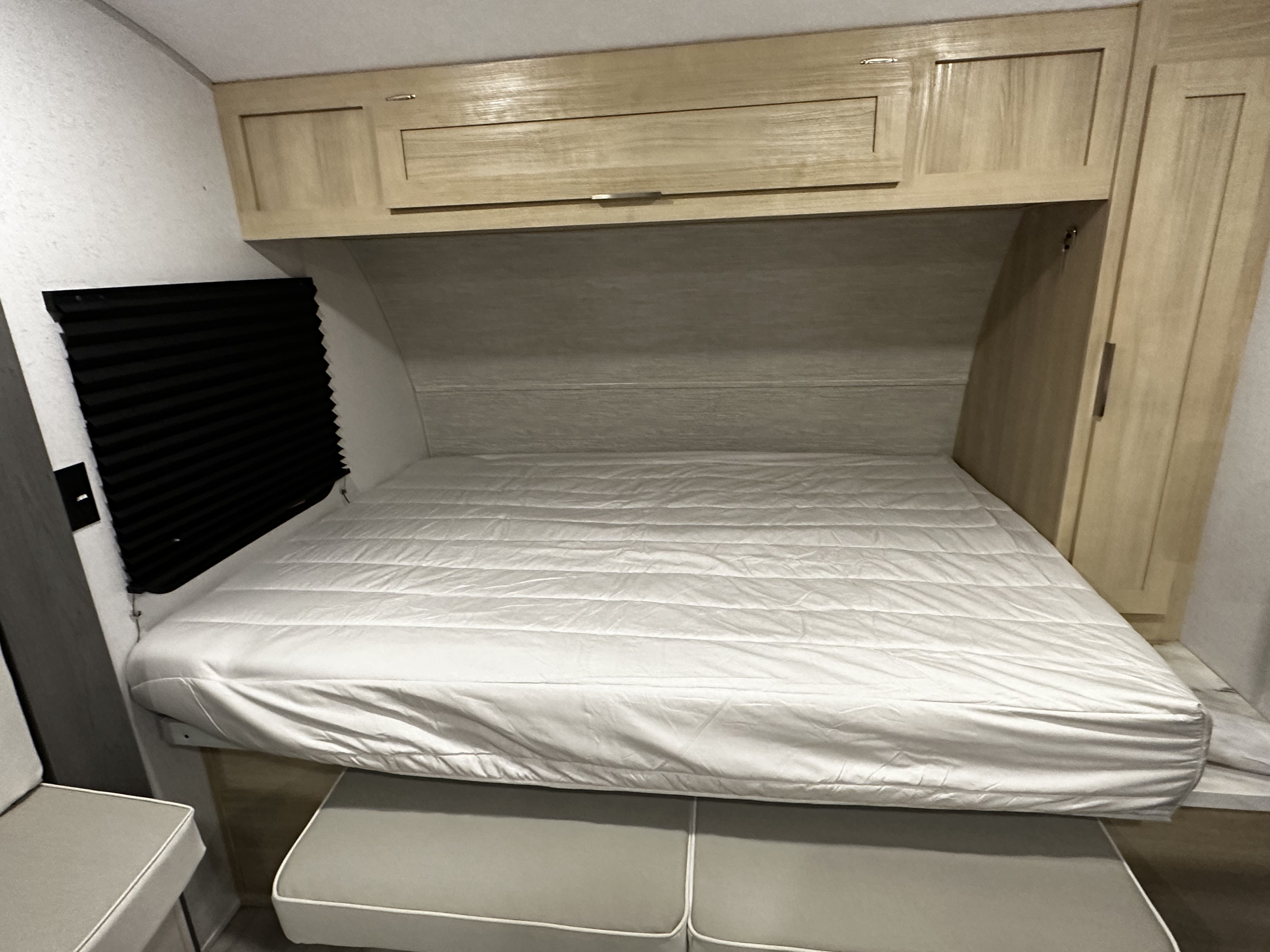 Cozy RV rental bedroom with a white mattress, light wood overhead cabinets, and a black pleated window blind.. Forest River Salem FSX Platinum 2023