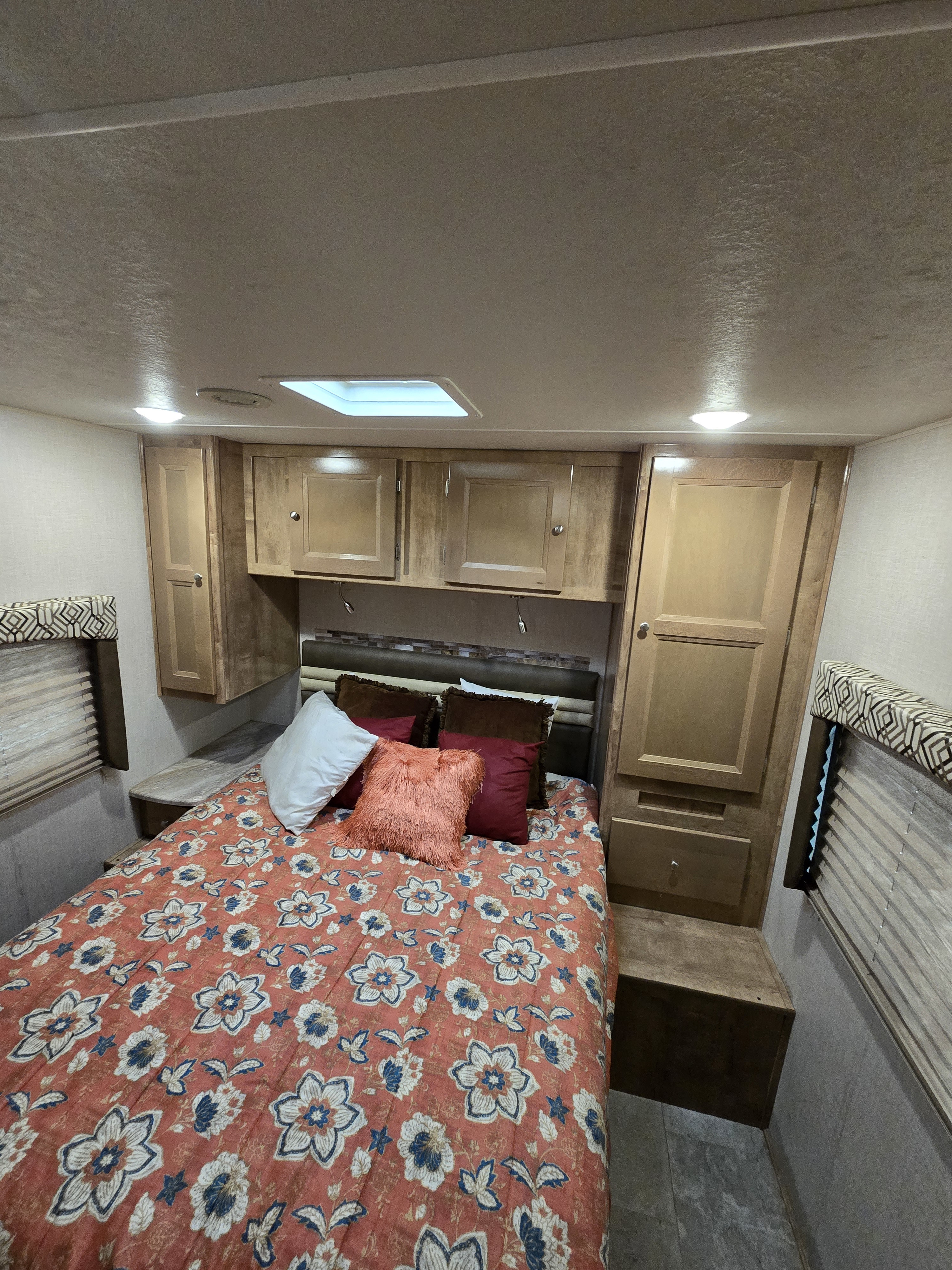 Cozy RV rental bedroom featuring a bed with floral bedding, built-in wooden cabinets, and bright overhead lighting.. Forest River Coachmen Leprechaun 2020