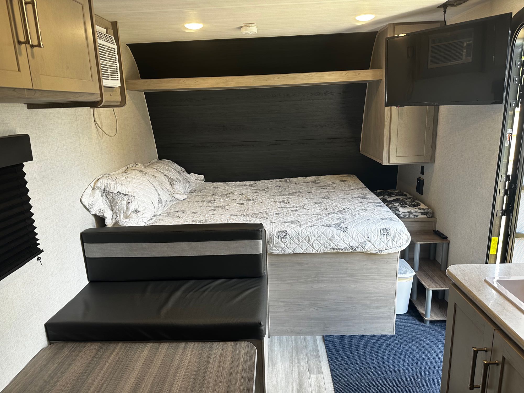 Cozy rv rental interior: features a comfy bed, dining/seating area, small kitchen, wall-mounted TV, and an AC unit.. Keystone Springdale 2024