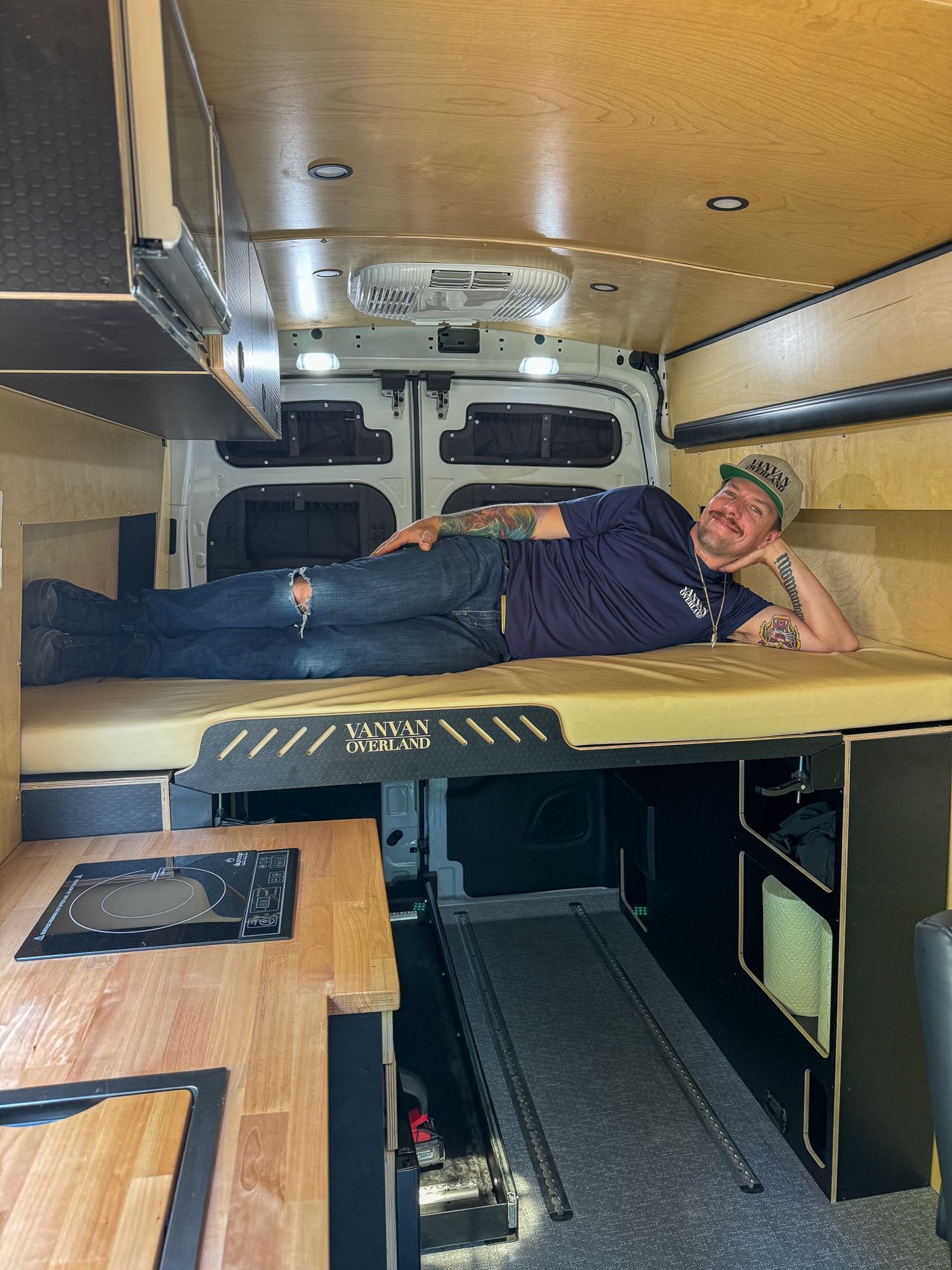 Inside an RV rental, a man relaxes in a custom camper van with a cozy bed & kitchen.. Ford Transit 2023