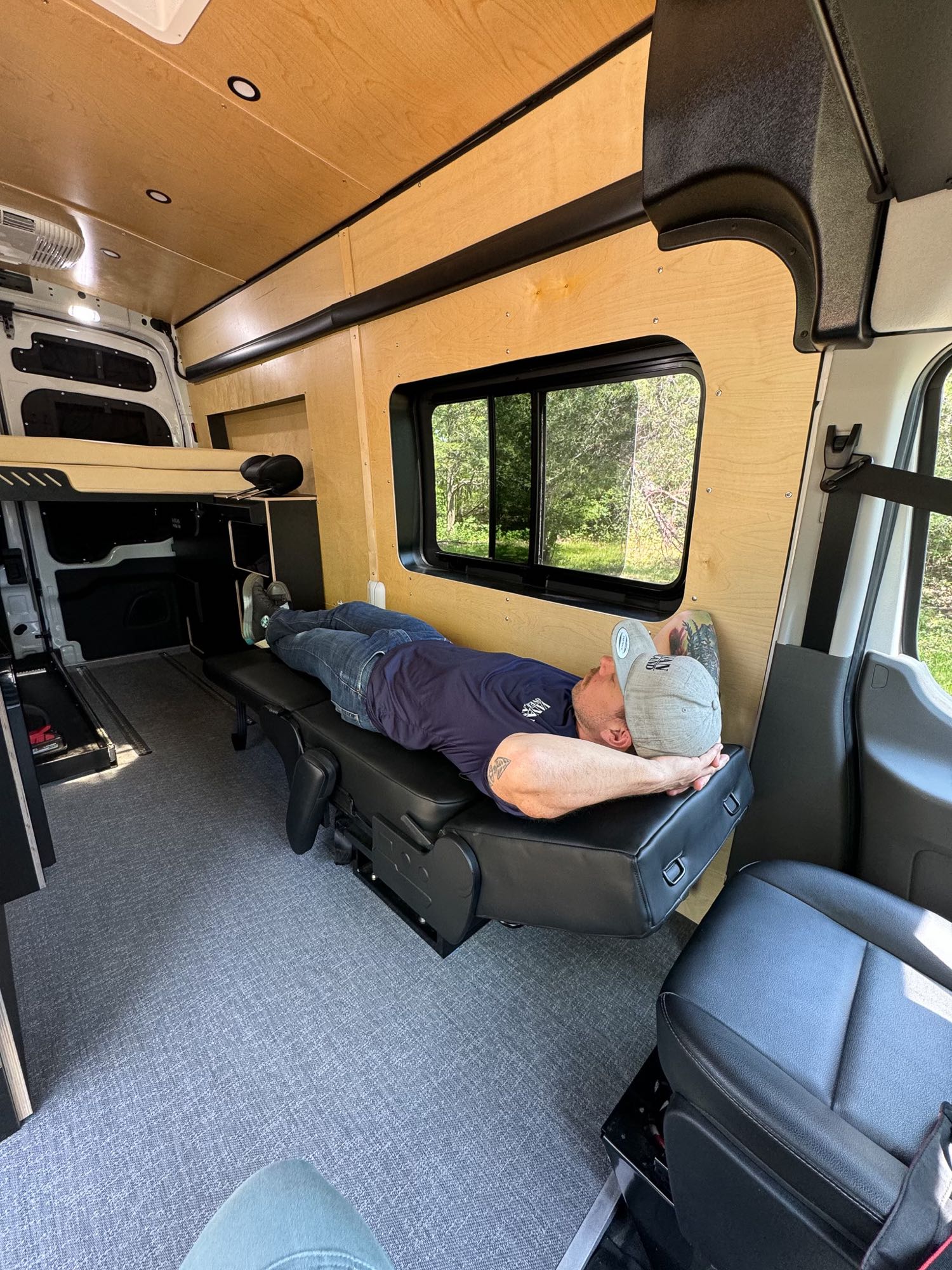Inside an RV rental: Man relaxes on a modular seat in this custom camper van conversion.. Ford Transit 2023