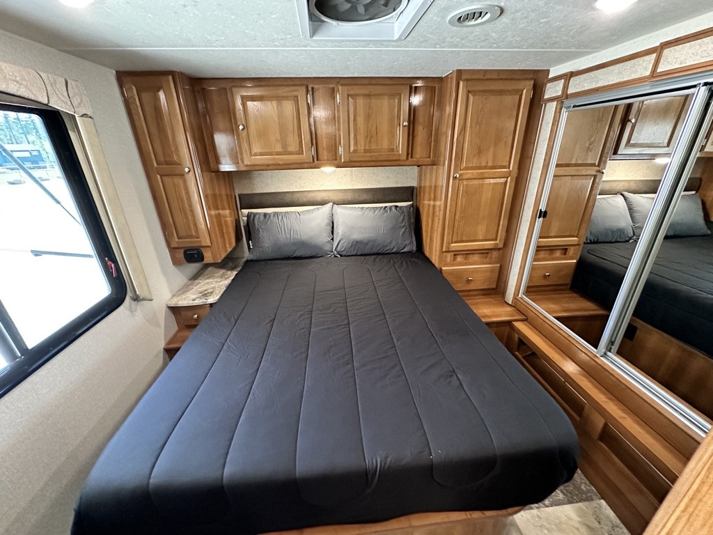 Cozy RV rental bedroom features a comfy bed, wooden cabinetry, and mirrored wardrobe for travel comfort.. Coachmen Leprechaun 2019