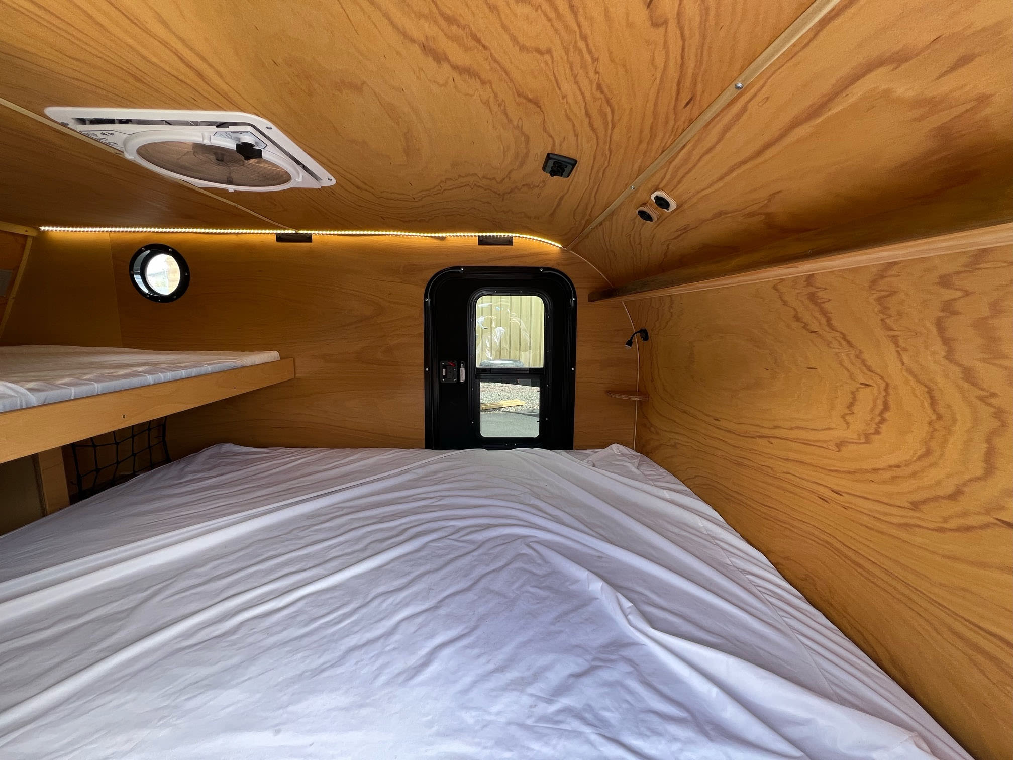 Inside a comfortable RV rental, featuring warm wood paneling, bunk beds, a ceiling fan, and LED lighting. Ideal for travel.. Bend Teardrop Inc. 6x12 2023