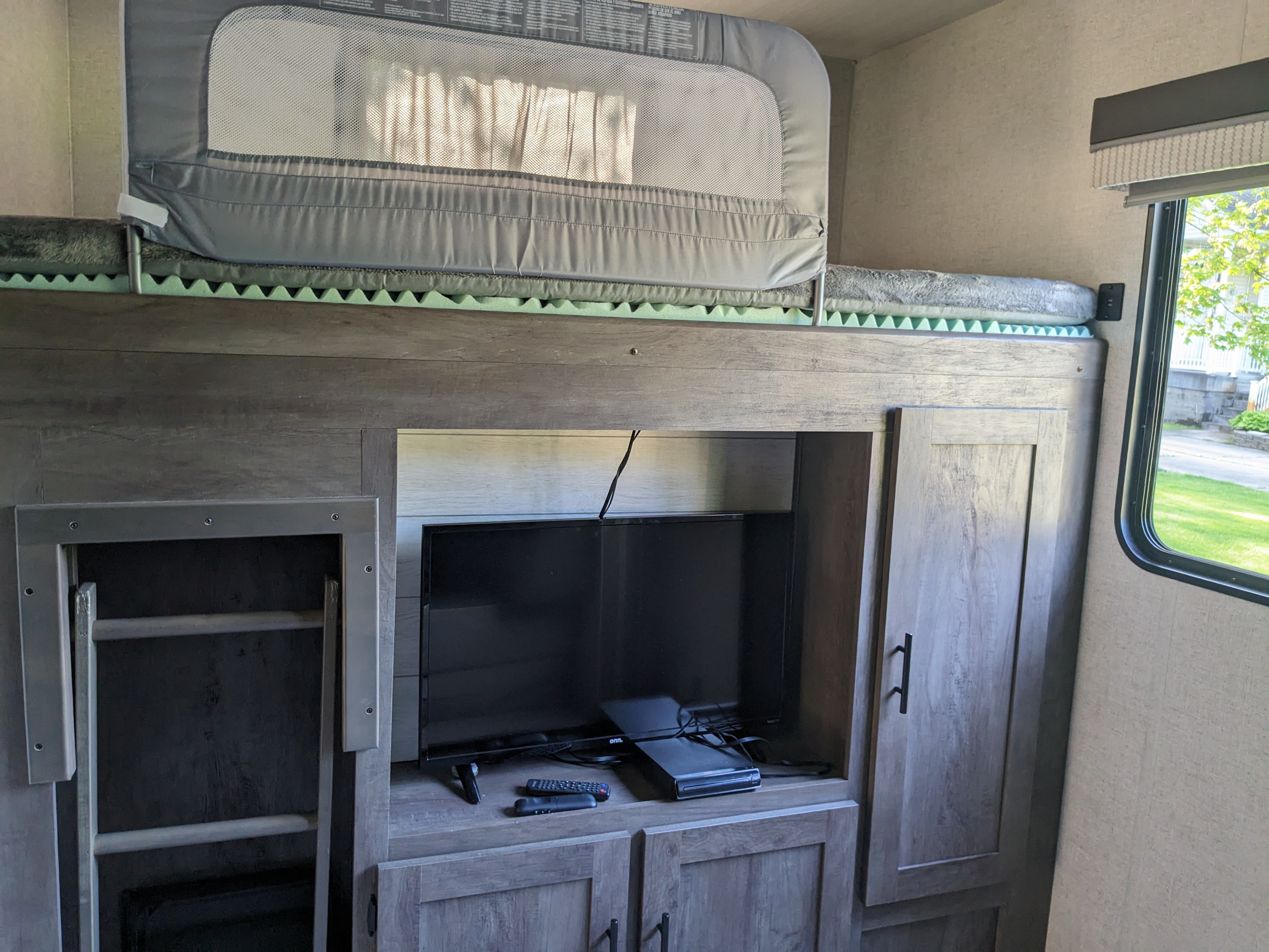 RV rental interior featuring a cozy bunk bed with a safety rail, an entertainment center with TV, and storage.. Forest River Wildwood 2021