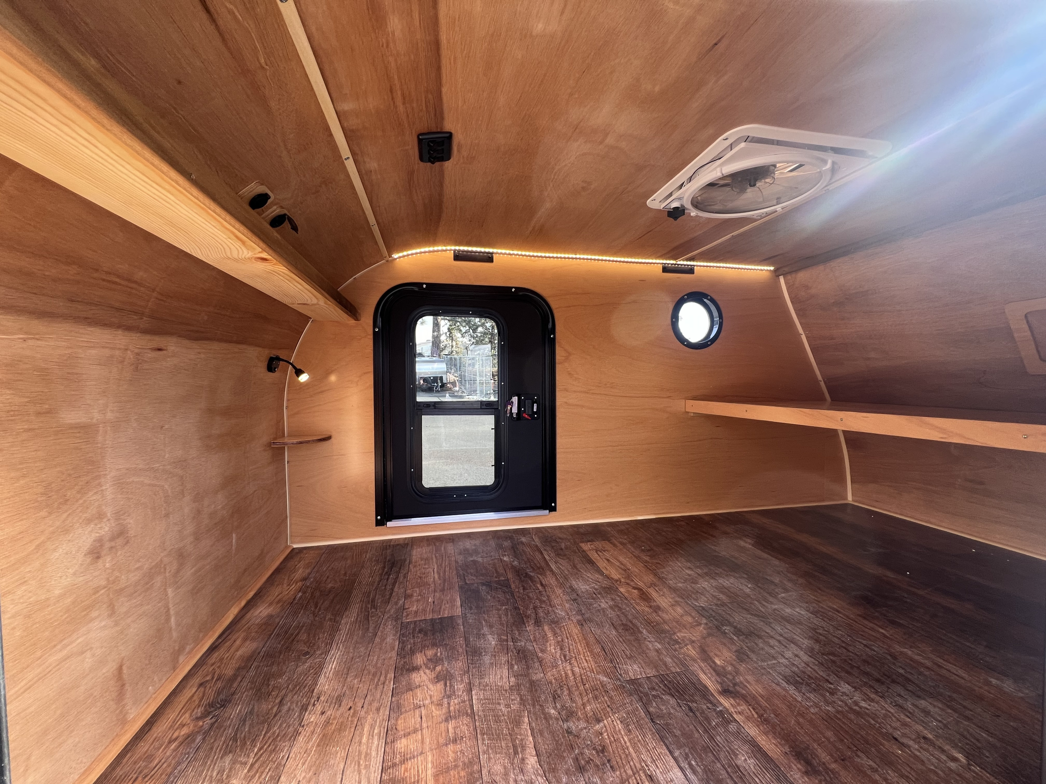 Cozy wood-paneled interior of an RV rental, featuring a door, windows, LED lighting, and a vent fan.. Bend Teardrop Inc. 6x12 2023