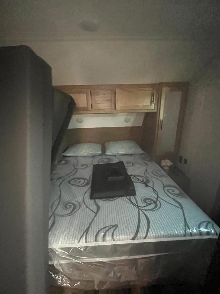 RV rental travel trailer bedroom. Features a bed with a patterned, protected mattress, two pillows, overhead cabinets, and a side closet.. Forest River Cherokee 2023