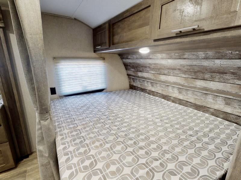 RV rental bedroom: comfortable bed with modern pattern, wood-paneled wall, overhead cabinets, and window blind.. Forest River Xlr Thunrderbolt 2022