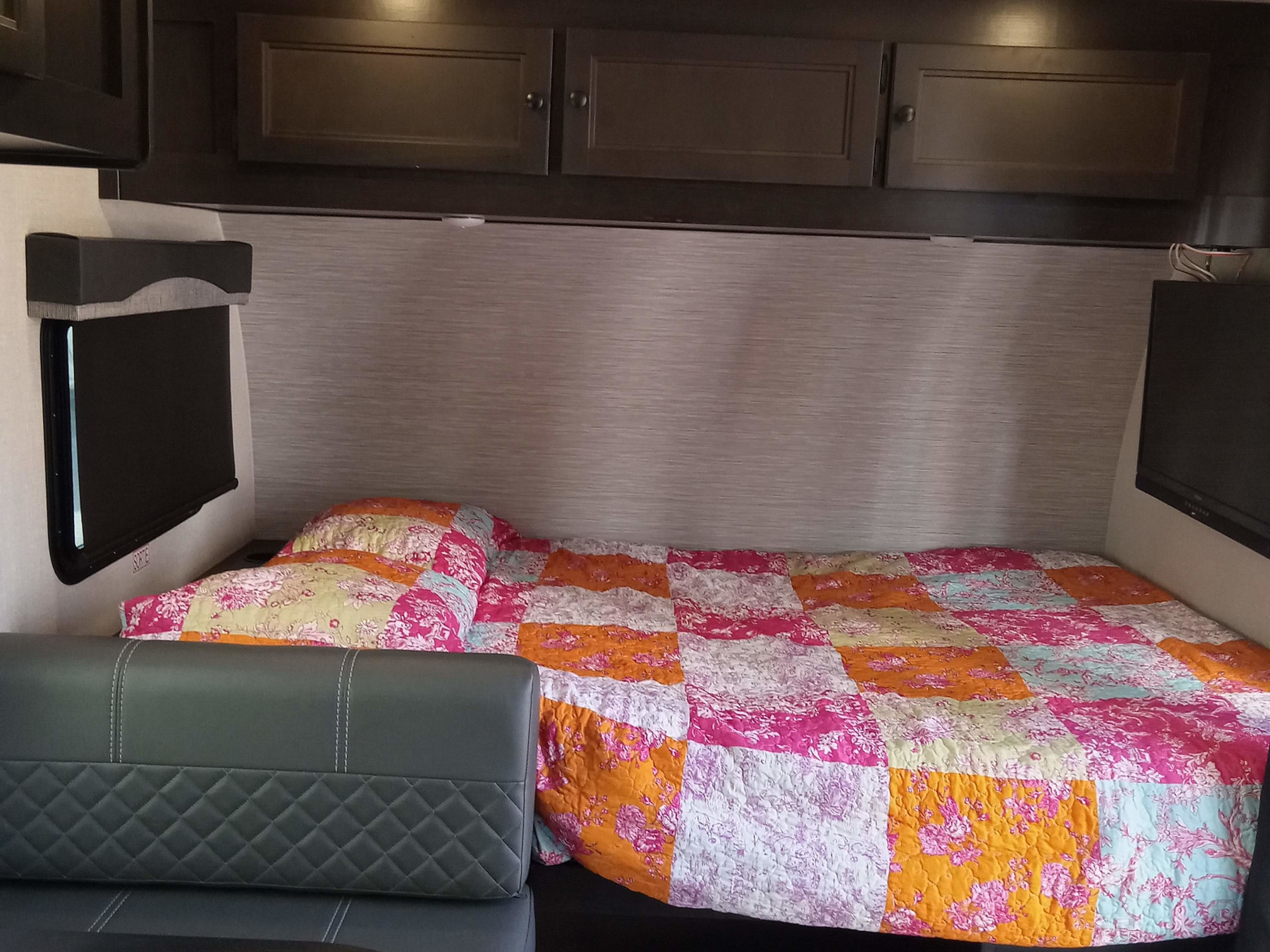 RV rental bedroom features a bright patchwork quilt on the bed, window, and storage for a cozy stay.. Highland Ridge RV Open Range 2022