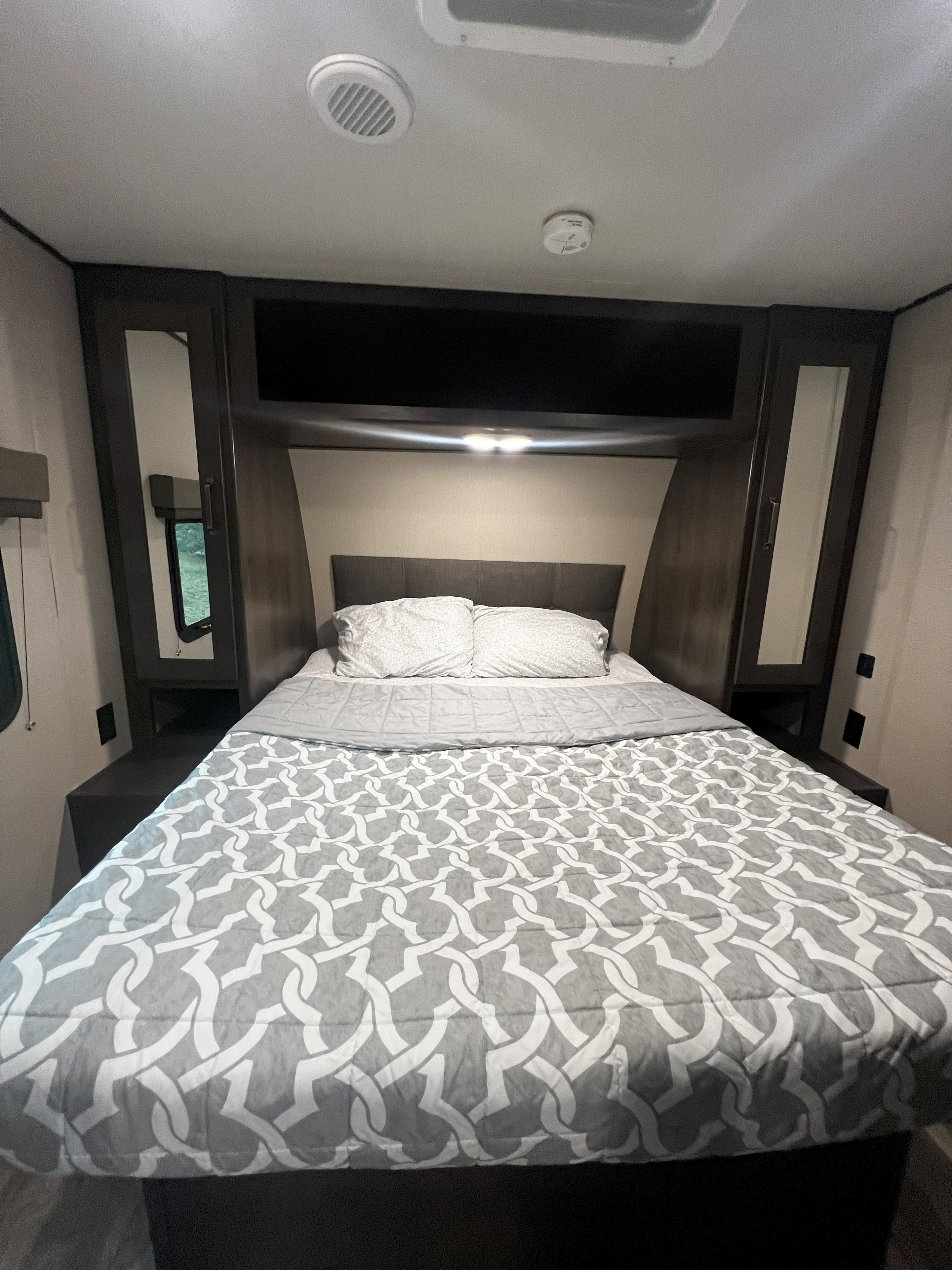 Comfortable RV rental bedroom featuring patterned bedding, built-in storage, a window, and ceiling vents.. Grand Design Transcend Xplor 265BH 2021