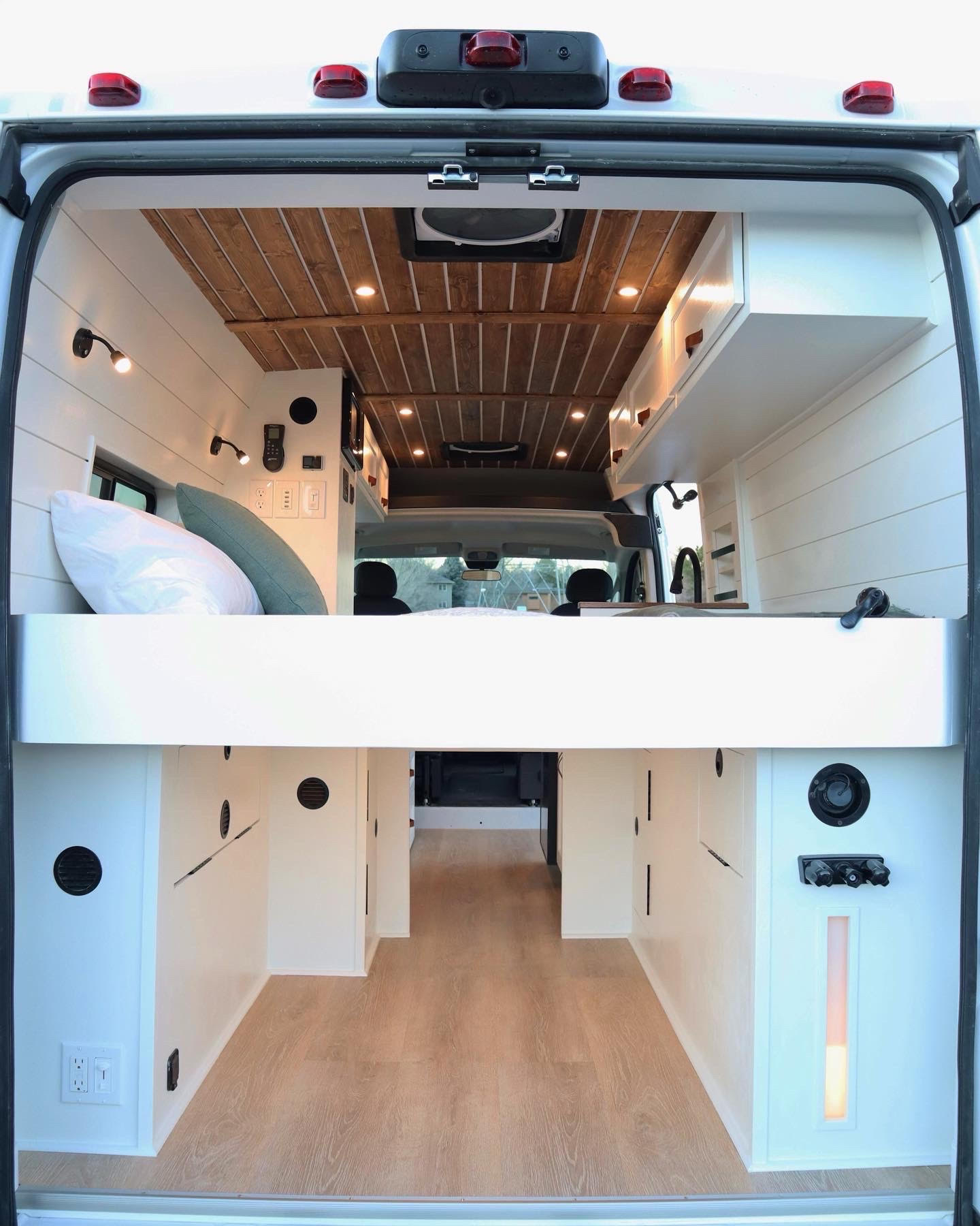 Spacious & modern camper van interior, viewed from the rear, featuring an elevated bed & ample storage. Ideal for RV rental.. RAM Promaster 2300 2023