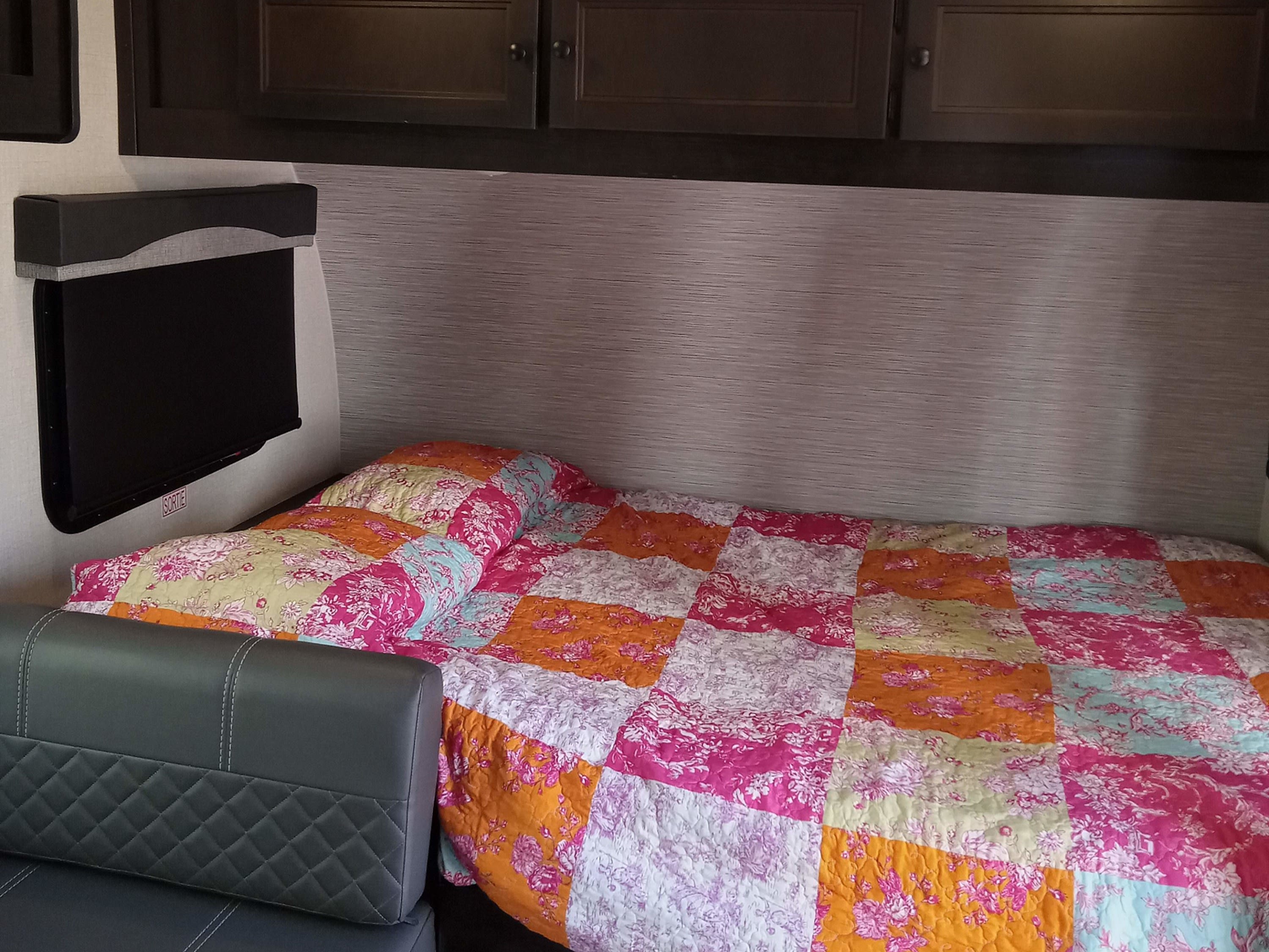Comfortable RV rental interior: colorful patchwork quilt on bed, cozy seating, exit window, and cabinets.. Highland Ridge RV Open Range 2022