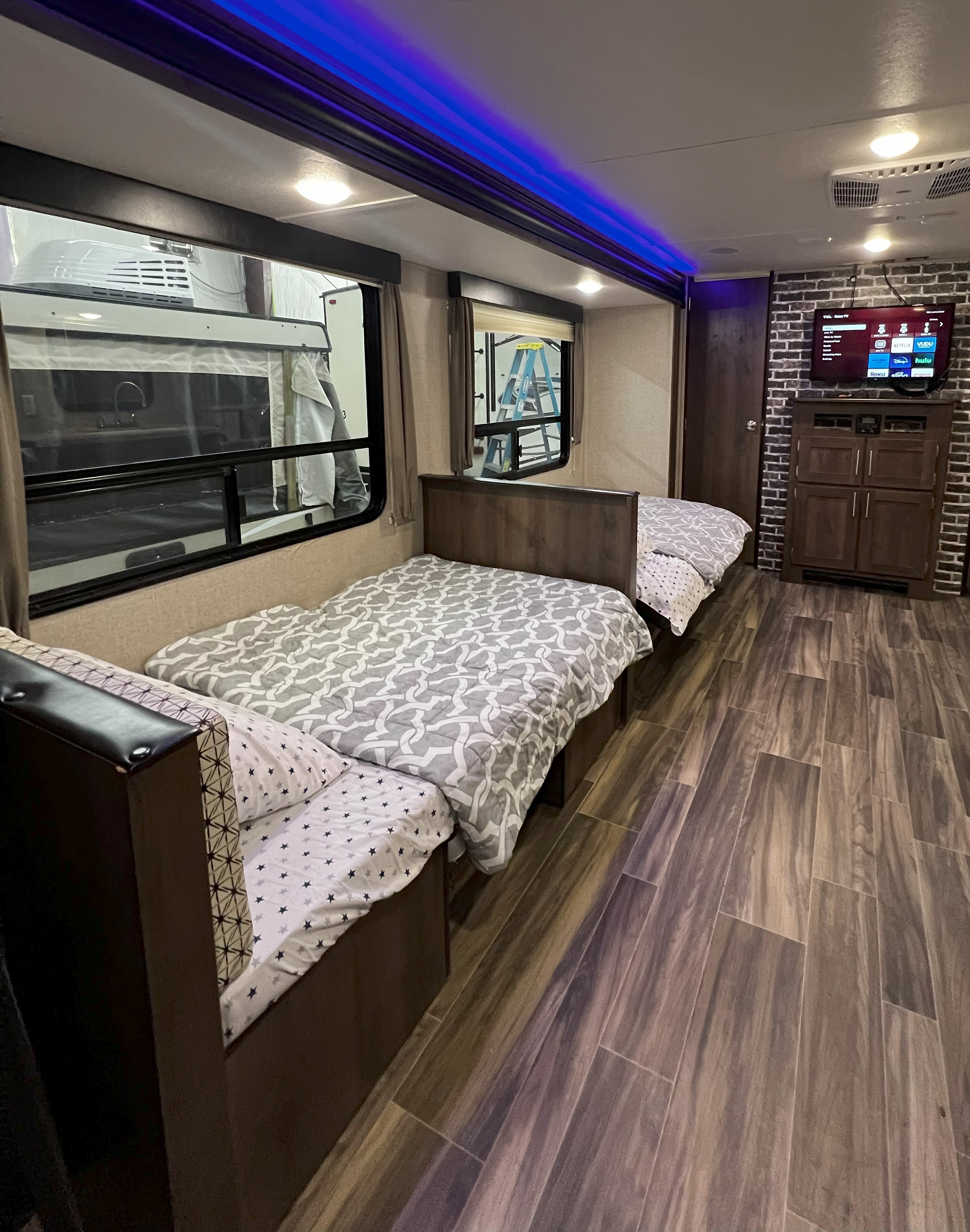 Inside a modern RV rental: two compact beds, TV on a faux brick wall, and blue accent lighting.. Forest River Shasta 26DB 2020