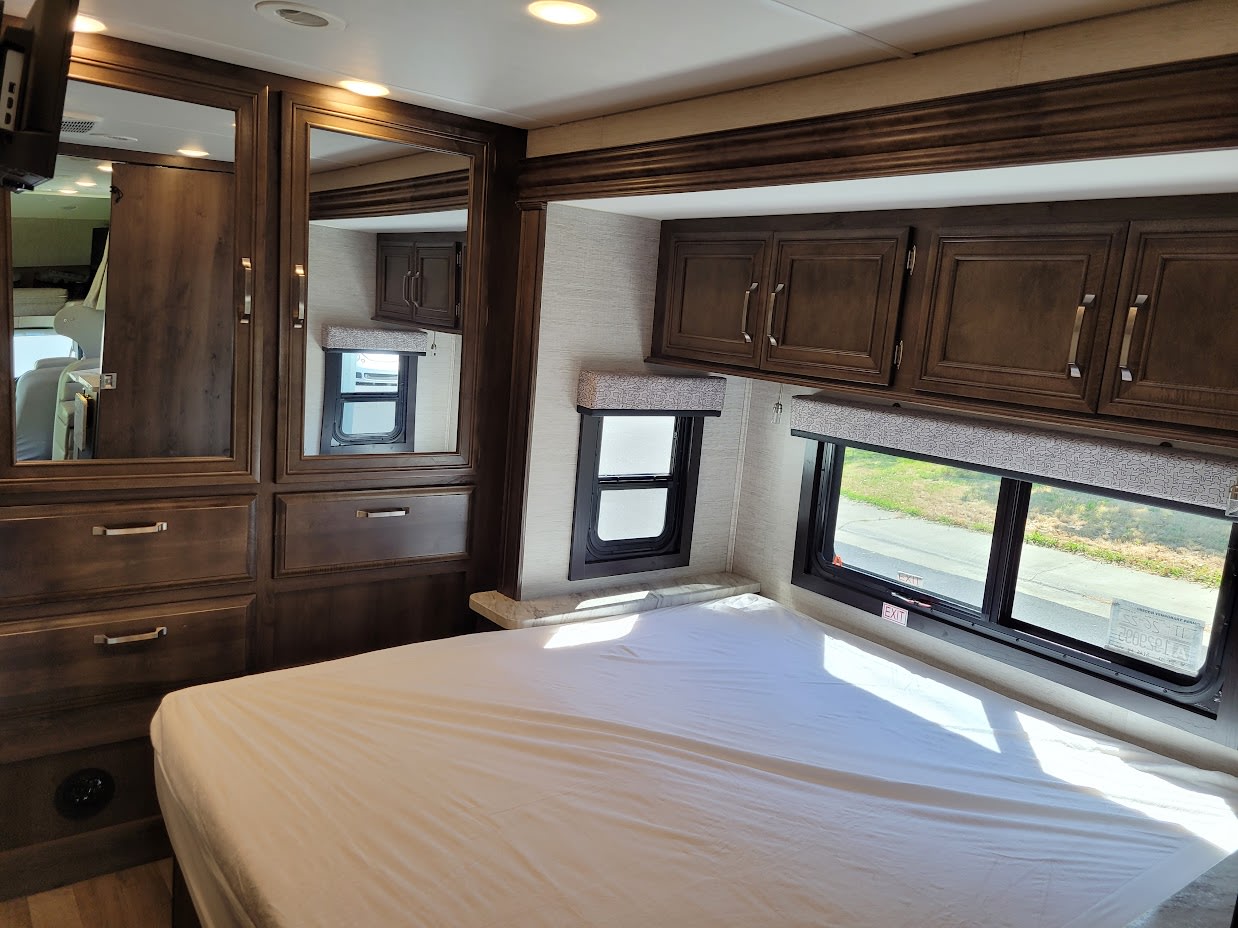 Spacious RV rental bedroom interior, featuring a comfortable bed, overhead cabinets, built-in storage, and large windows.. Jayco Greyhawk 2021