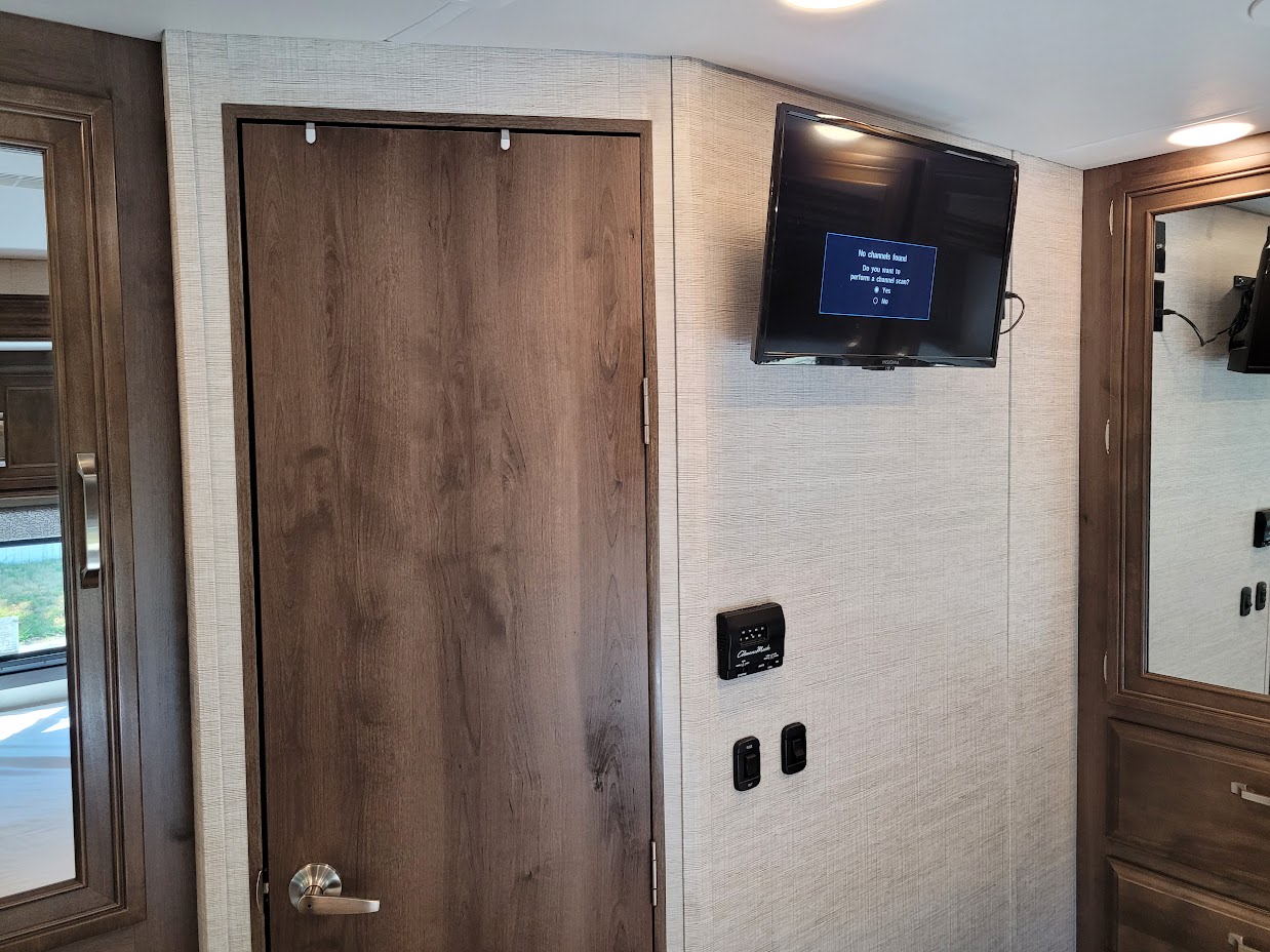 RV rental interior: A mounted TV displays "No channels found" message, alongside a wooden door and system controls.. Jayco Greyhawk 2021