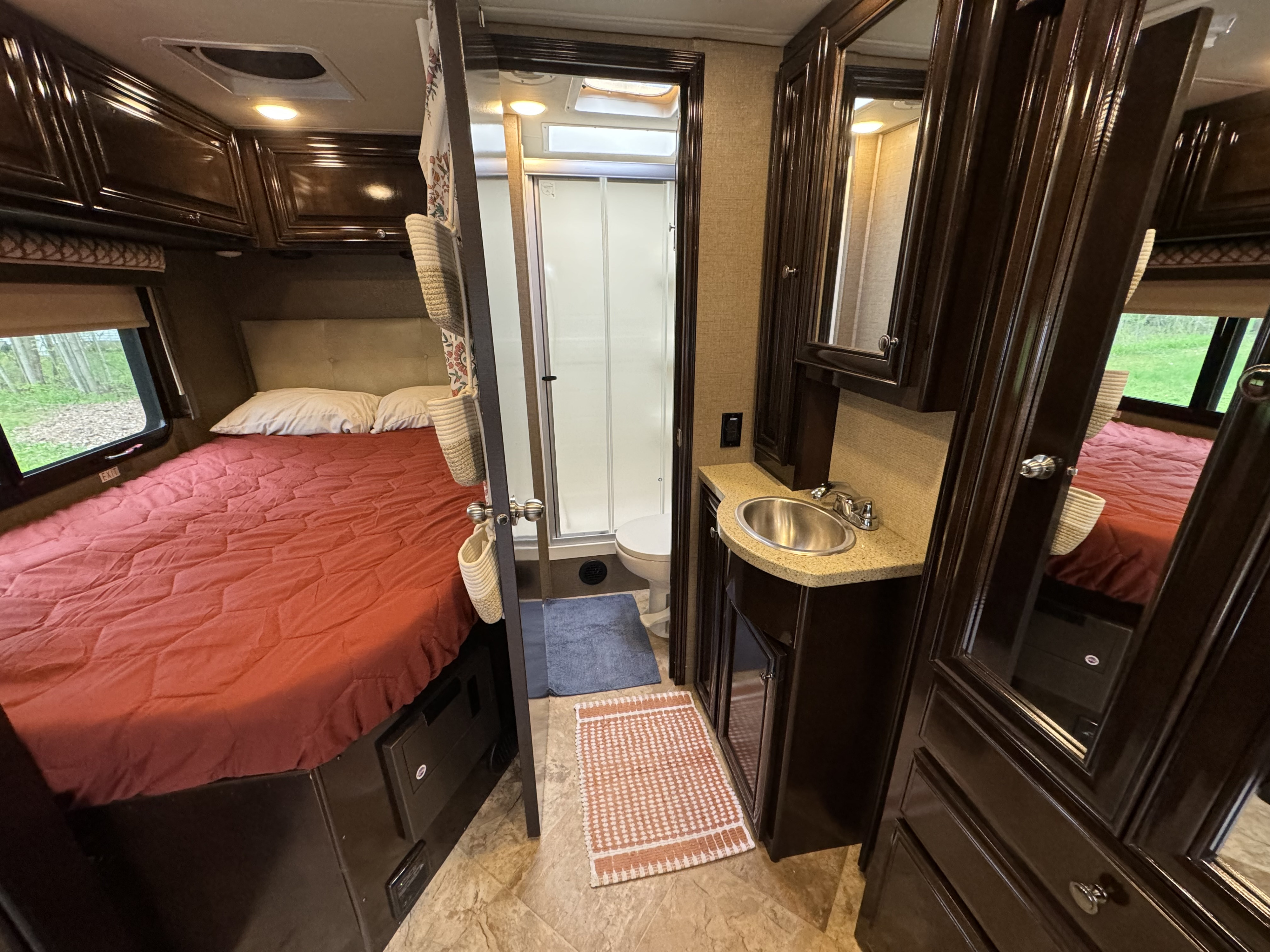 Inside an RV rental: a well-appointed bedroom with a red bed, and a compact bathroom including a sink and shower.. Thor Citation Sprinter 2018