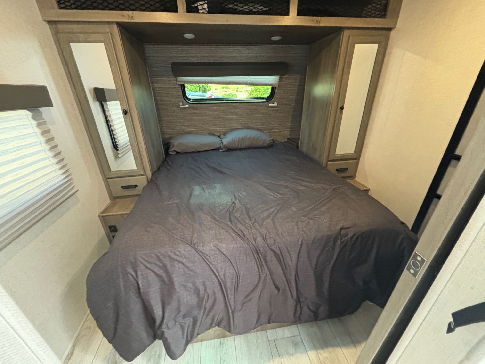 Comfortable RV rental bedroom with a cozy bed, side storage, overhead cabinets, and a window. Ideal for your road trip comfort.. Forest River 296 QBLE 2023