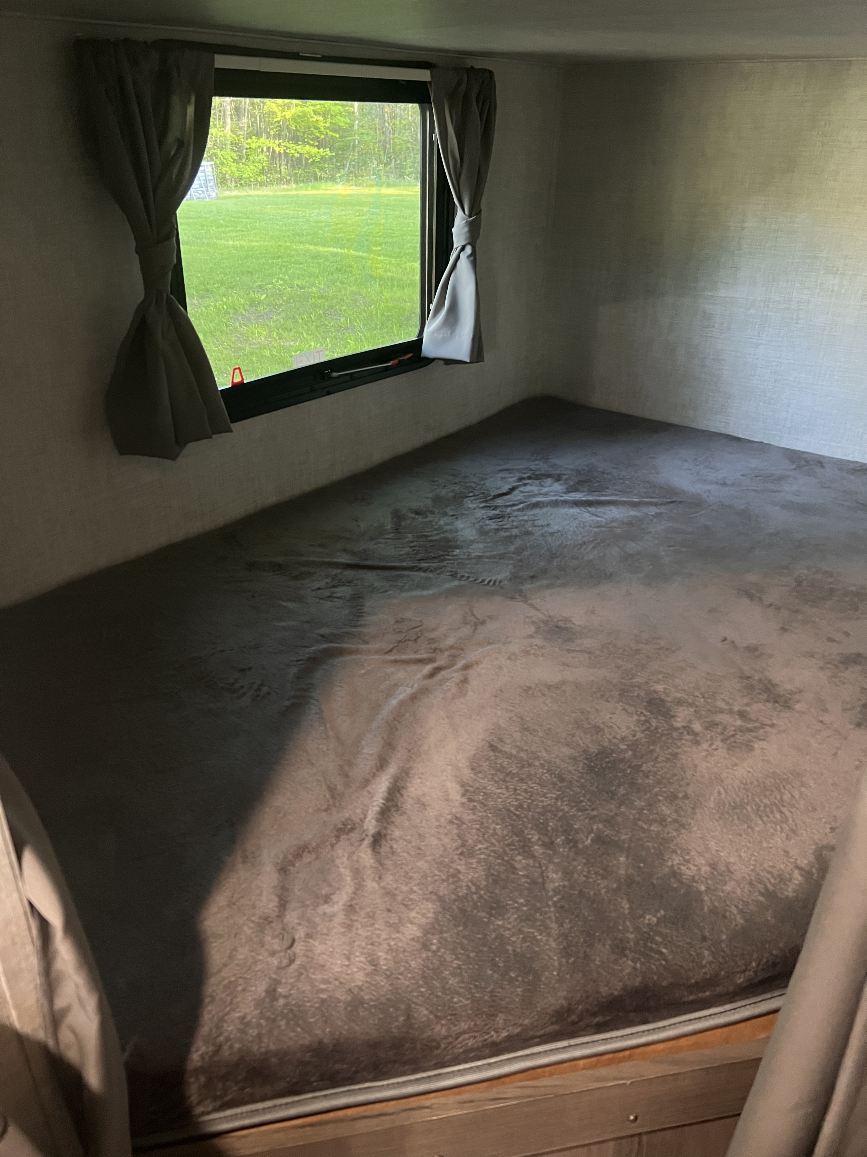 An RV rental's cozy bunk bed, featuring a window with open curtains looking out to a vibrant green outdoor scene.. Gulf Stream Ameri-Lite 2022