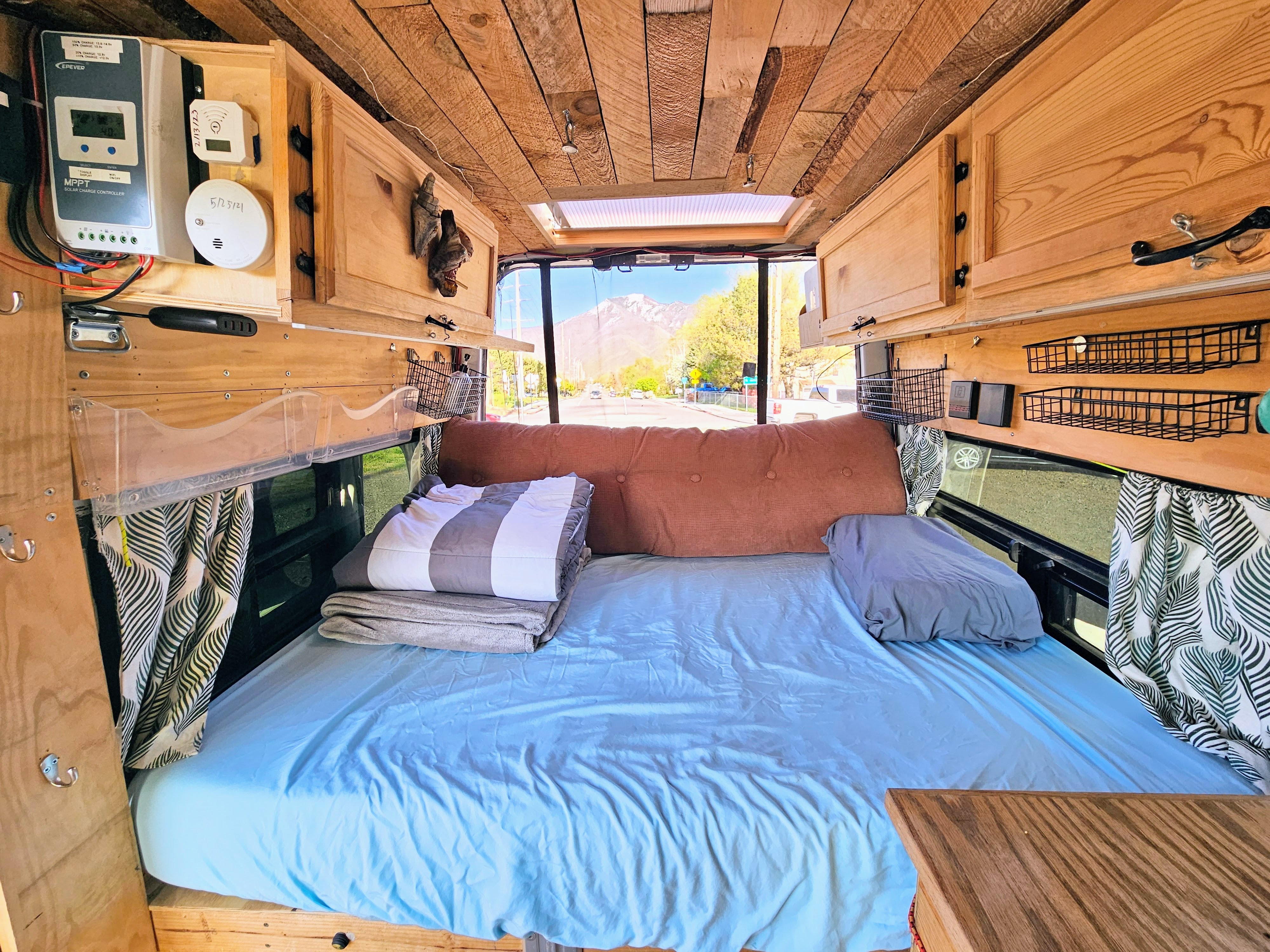 RV rental: Inside a custom camper, admire the cozy bed, wooden ceiling, solar setup, and mountain view outside.. Nissan Other 2012