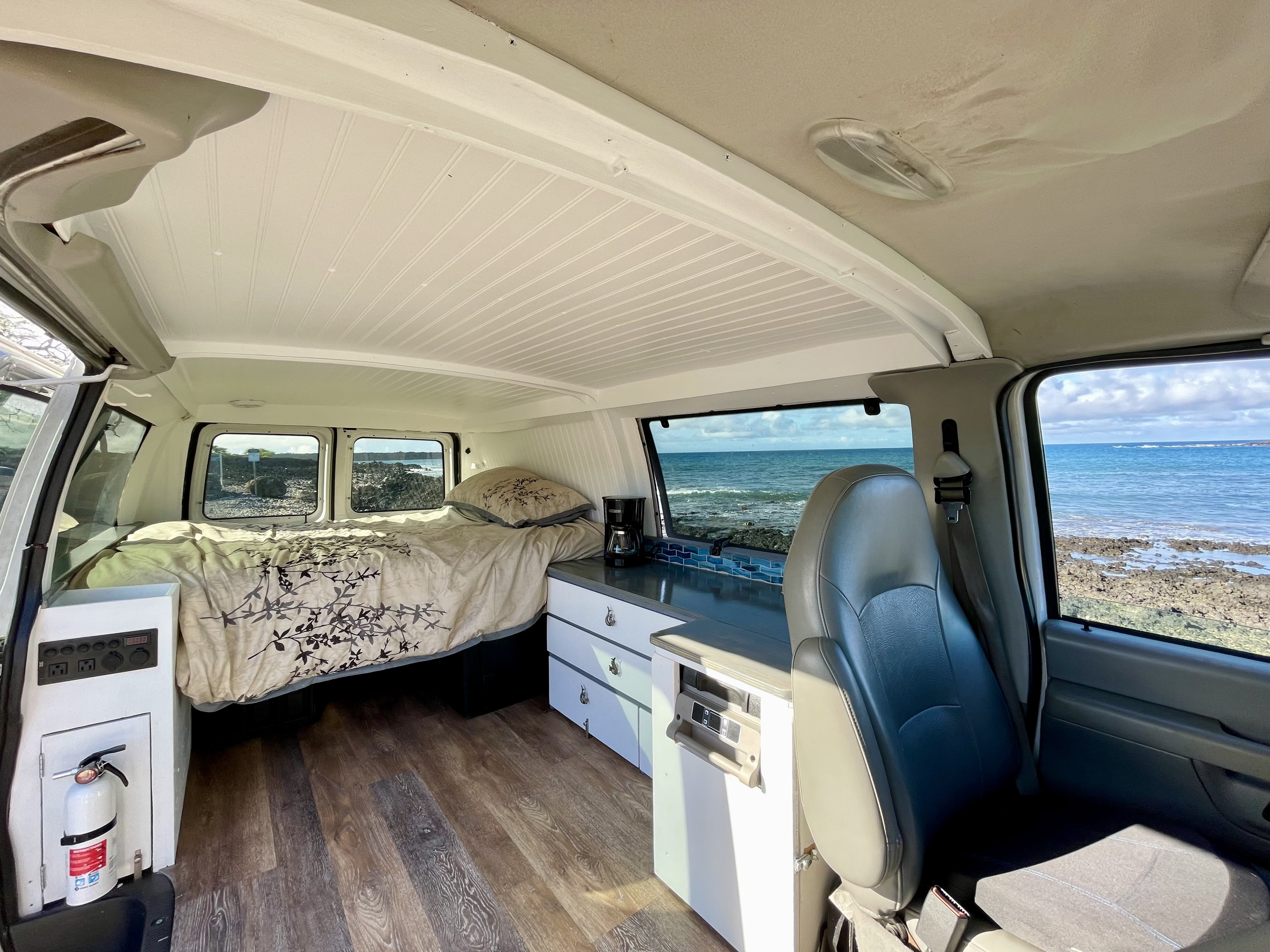 Cozy camper van interior with ocean view, perfect for an RV rental adventure. Features bed, kitchen, & scenic backdrop.. Ford Econoline 150 2007