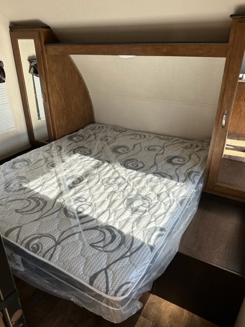 RV rental bedroom featuring a new mattress still in plastic, flanked by built-in wooden cabinetry and side mirrors.. Forest River Salem Cruise Lite 2023