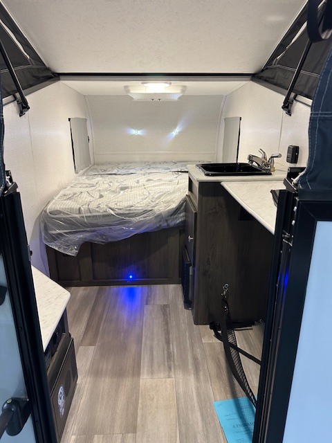 Inside a cozy rv rental: bedroom area with plastic-covered bed, small kitchen sink, and wood-style floor.. Viking 9.0TD 2022