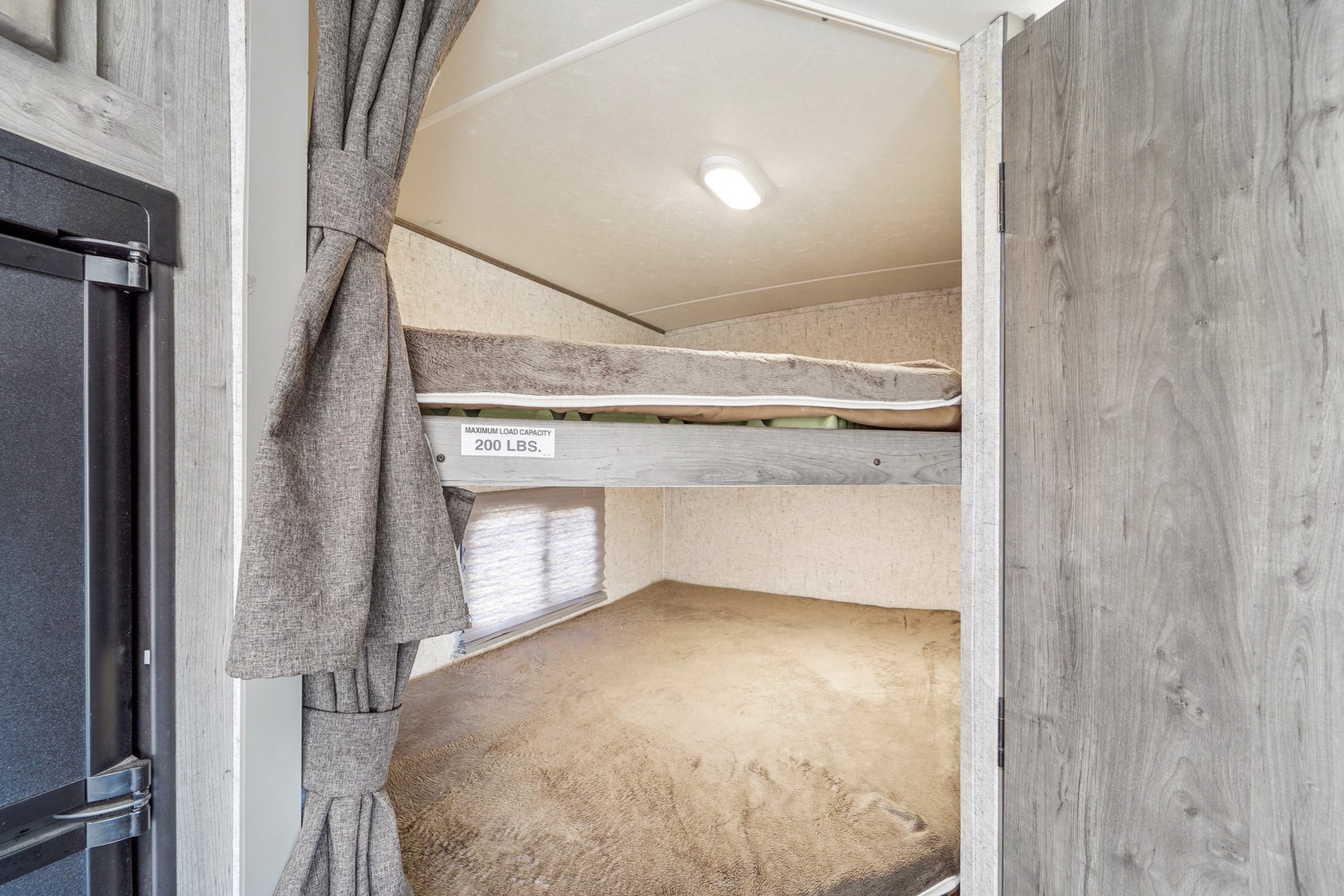 RV rental interior: Cozy bunk beds with a 200 lbs load capacity sign, light, and curtains, perfect for family travel.. Forest River Coachman Apex 2019