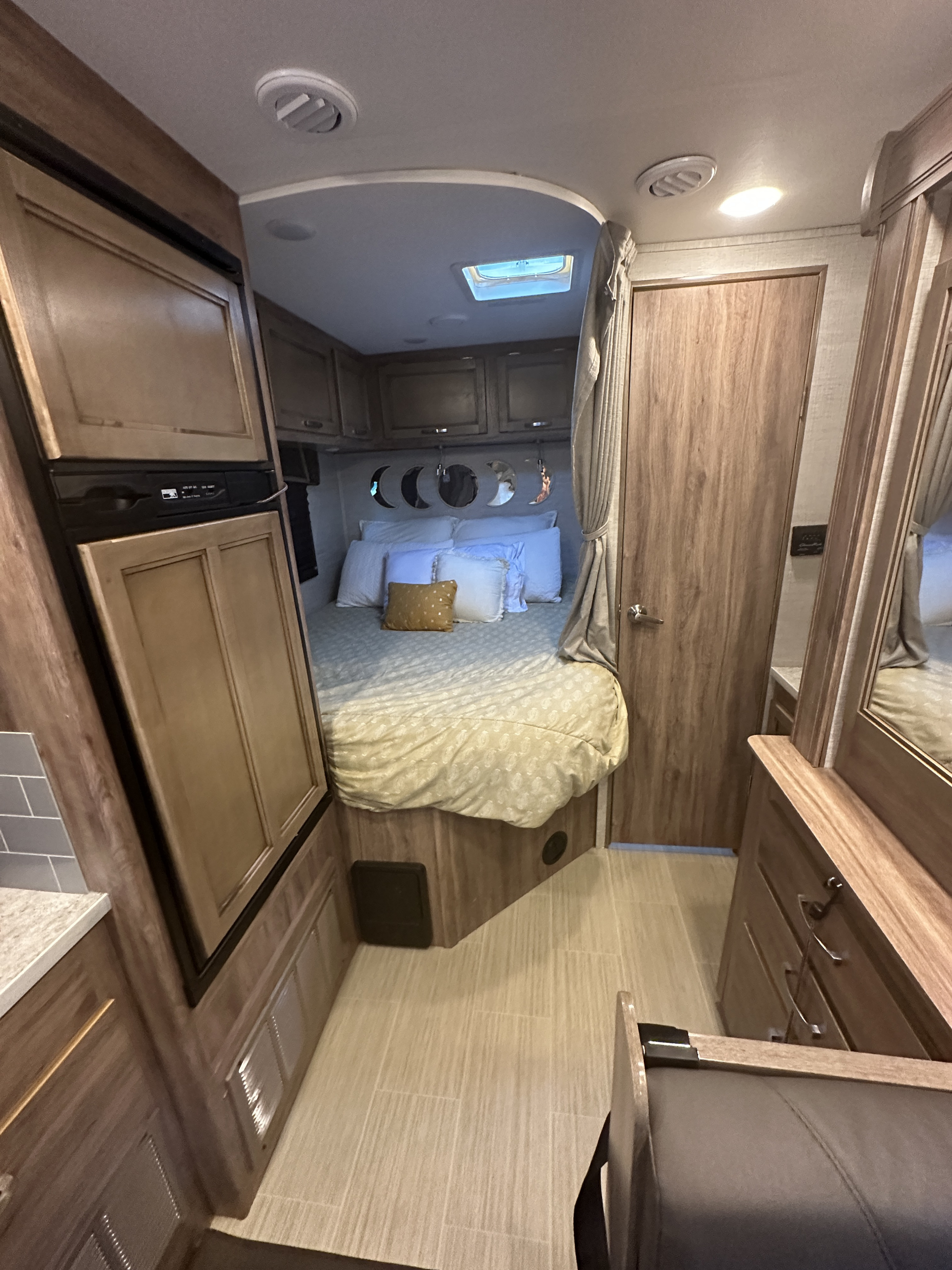 Step inside this RV rental, featuring a cozy bedroom with moon decor, a compact kitchen with a fridge, and efficient storage.. Jayco Redhawk SE 2021