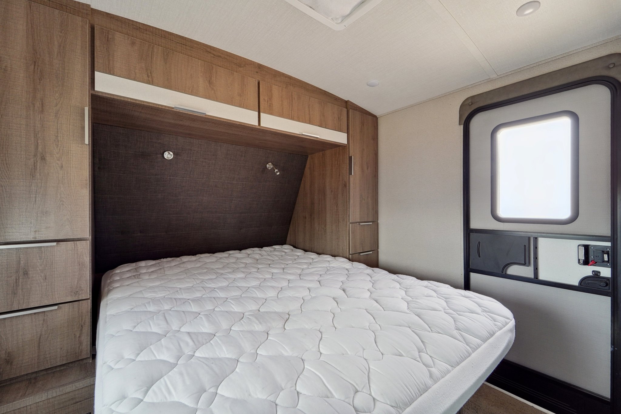Experience comfort in this RV rental bedroom featuring a large quilted bed, built-in storage, and an RV entrance door.. Grand Design Imagine 2021